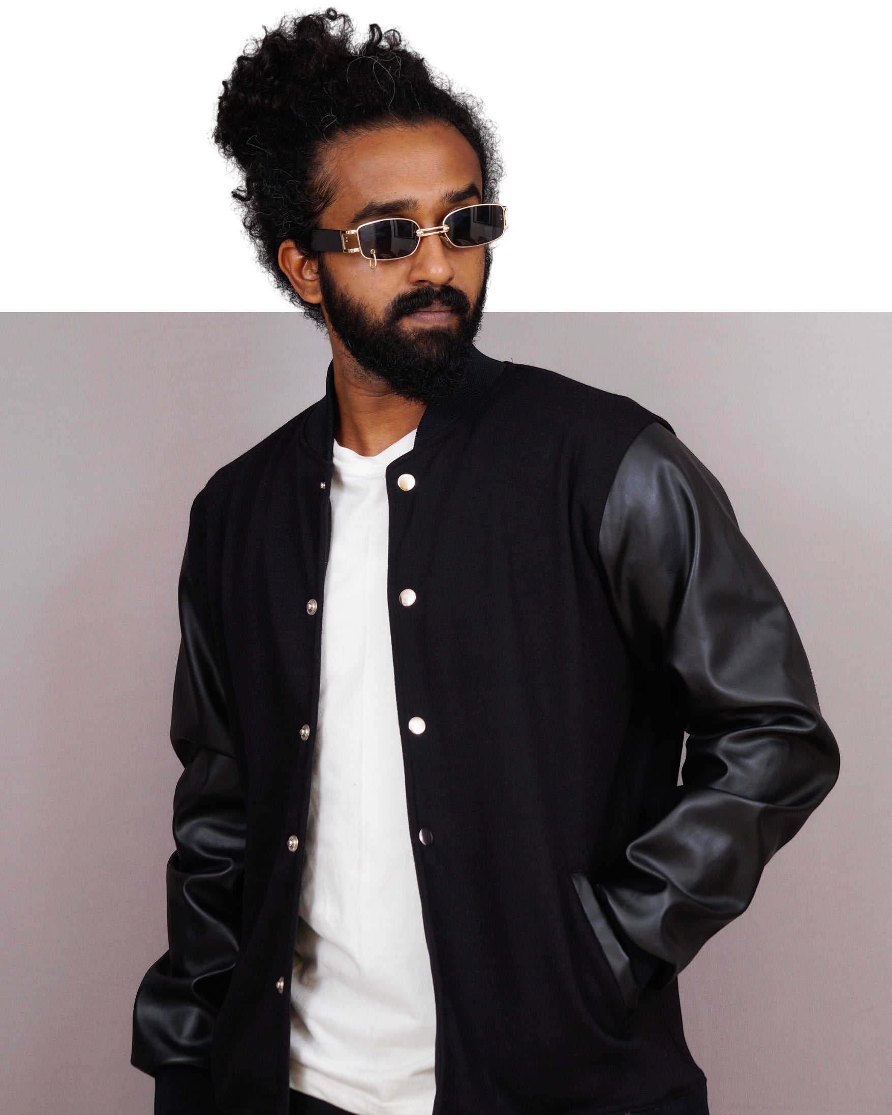 Man wearing a black varsity jacket with leather sleeves on a plain background