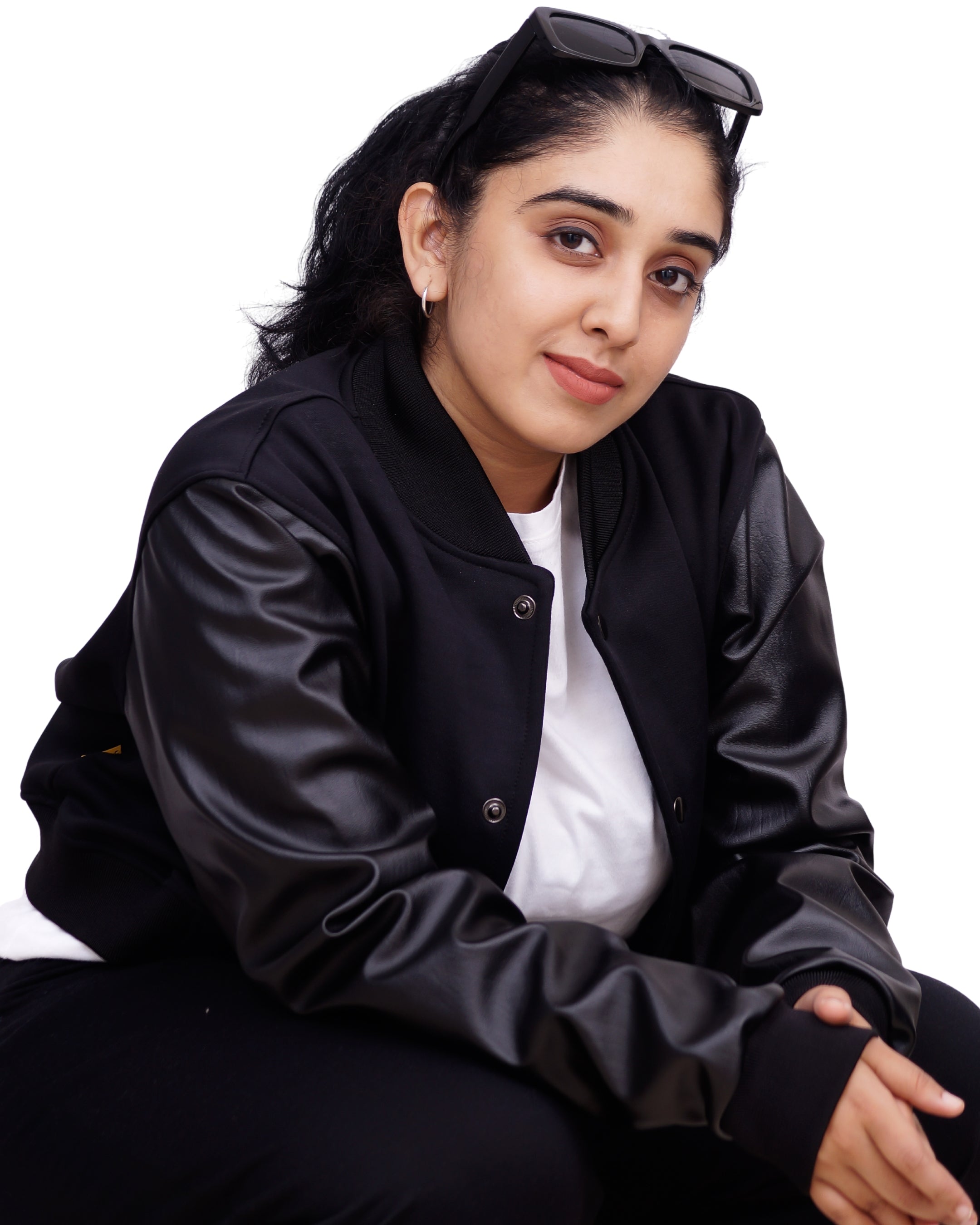 Person wearing a black jacket and white shirt with sunglasses on head, sitting against a white background
