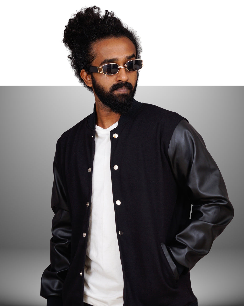 Man wearing a black varsity jacket over a white shirt with a gray background