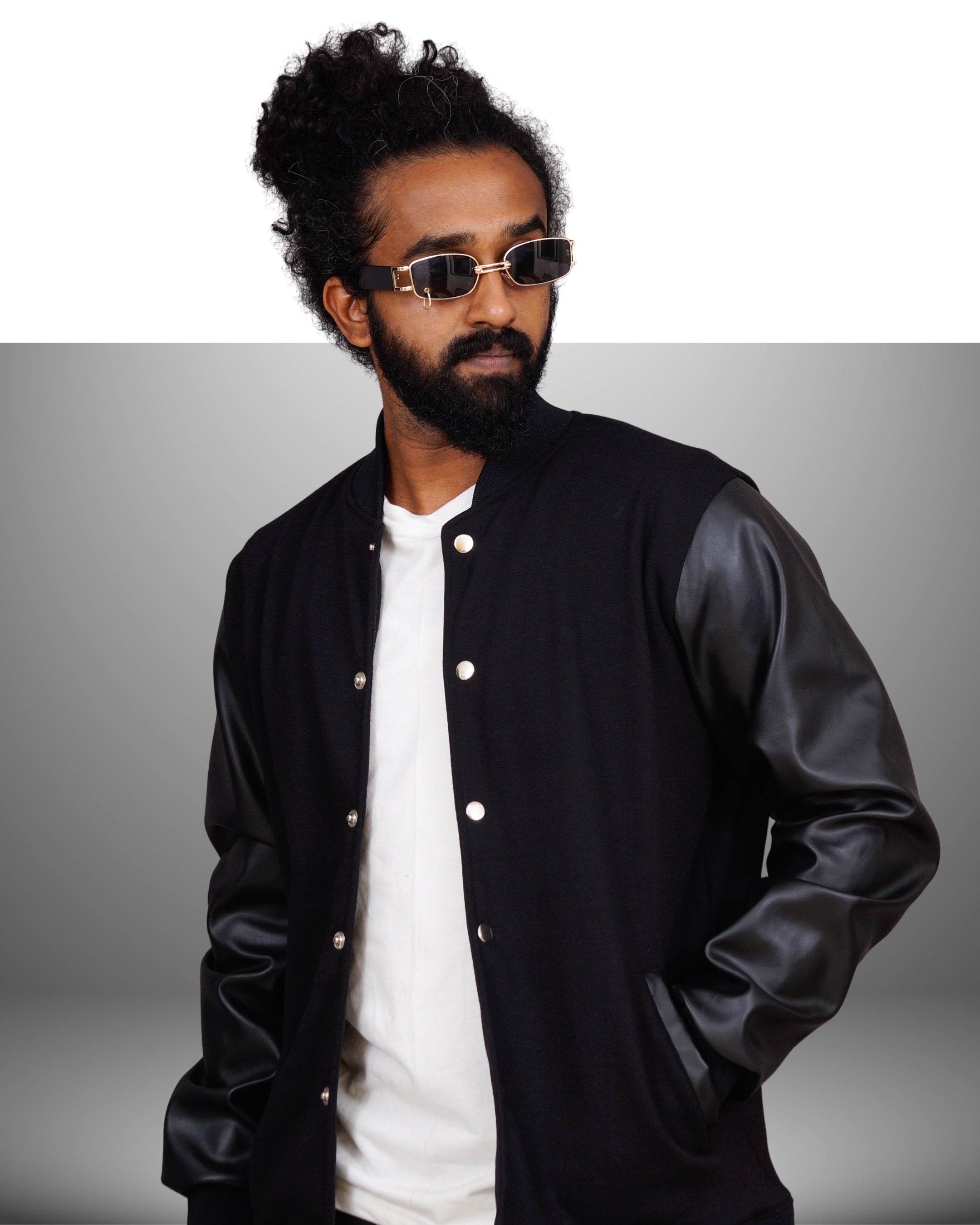 Man wearing a black varsity jacket over a white shirt with a gray background