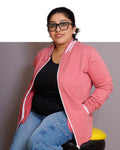 Person wearing a pink jacket with white trim, black top, and blue jeans on a gray background