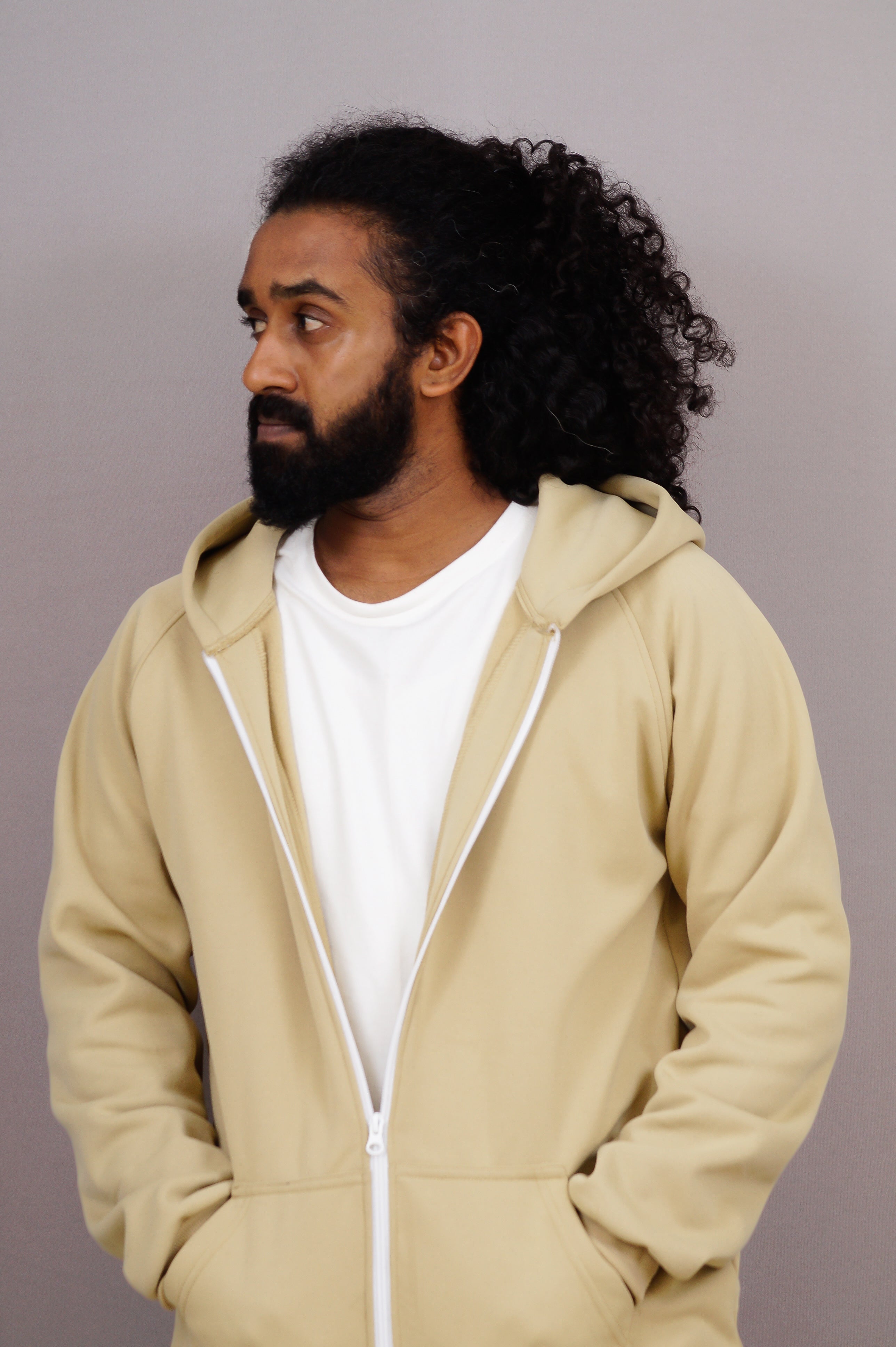 Man wearing a beige hoodie over a white shirt against a plain background