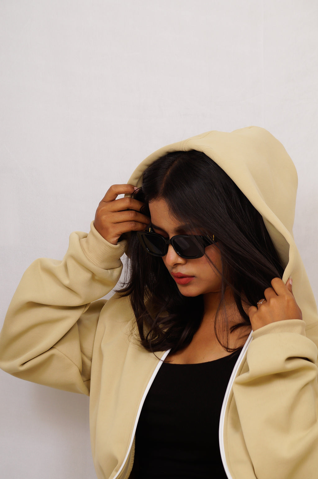 Person wearing a beige hoodie and sunglasses against a plain background
