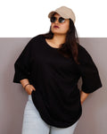 Person wearing a black oversized shirt, light blue jeans, and a beige cap with sunglasses on a plain background