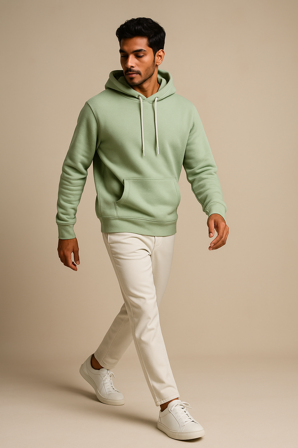 Man wearing a light green hoodie and white pants on a beige background