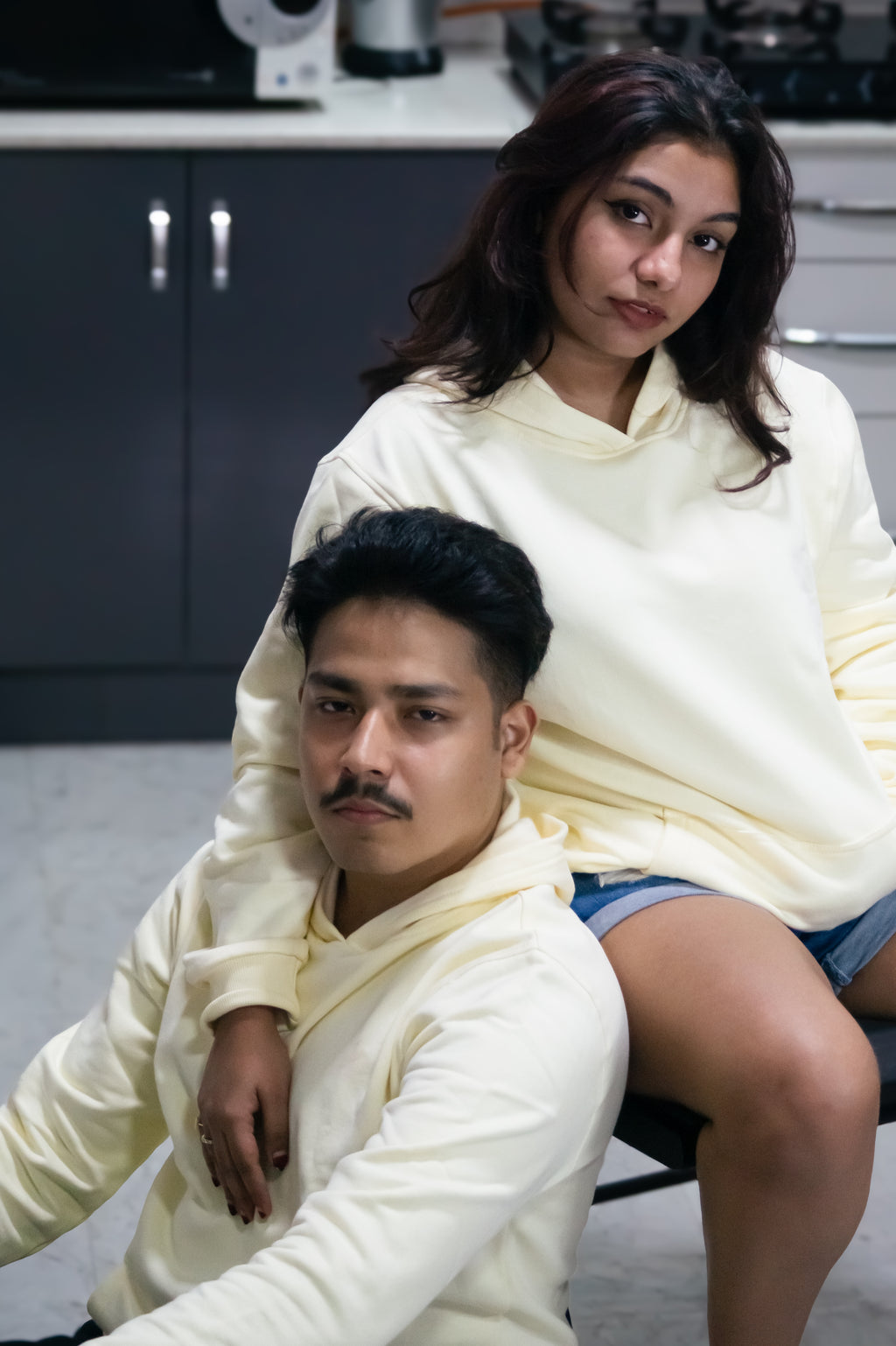 Two people wearing matching light-colored hoodies in a casual setting.