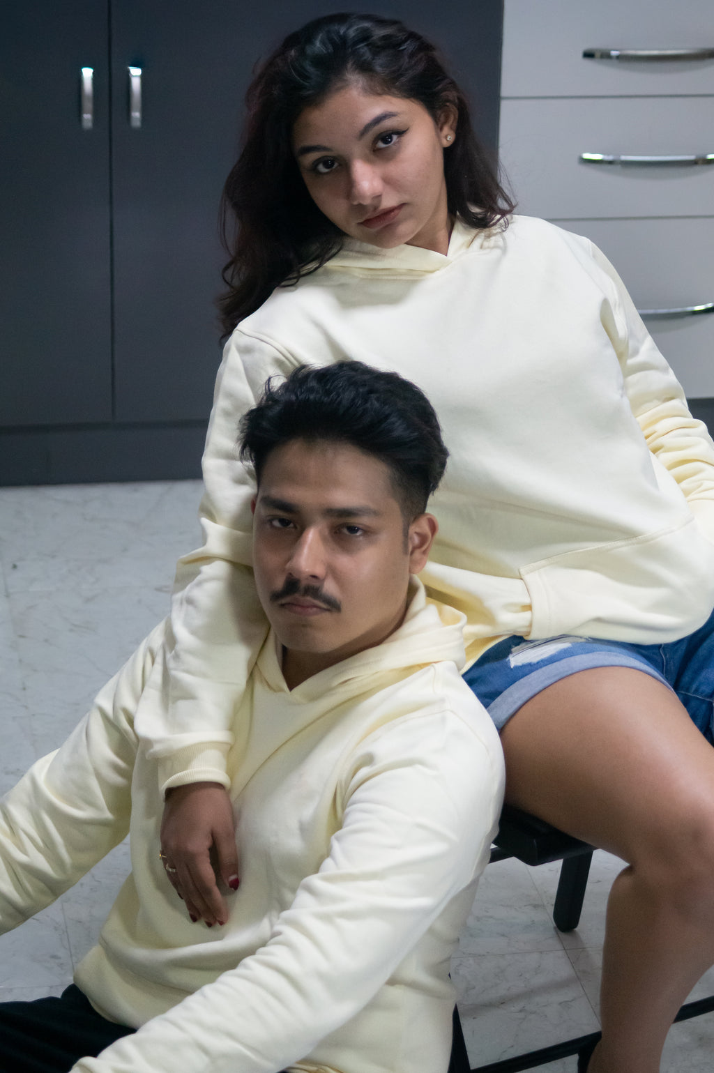 Two people wearing matching cream-colored sweaters in a room with gray cabinets.