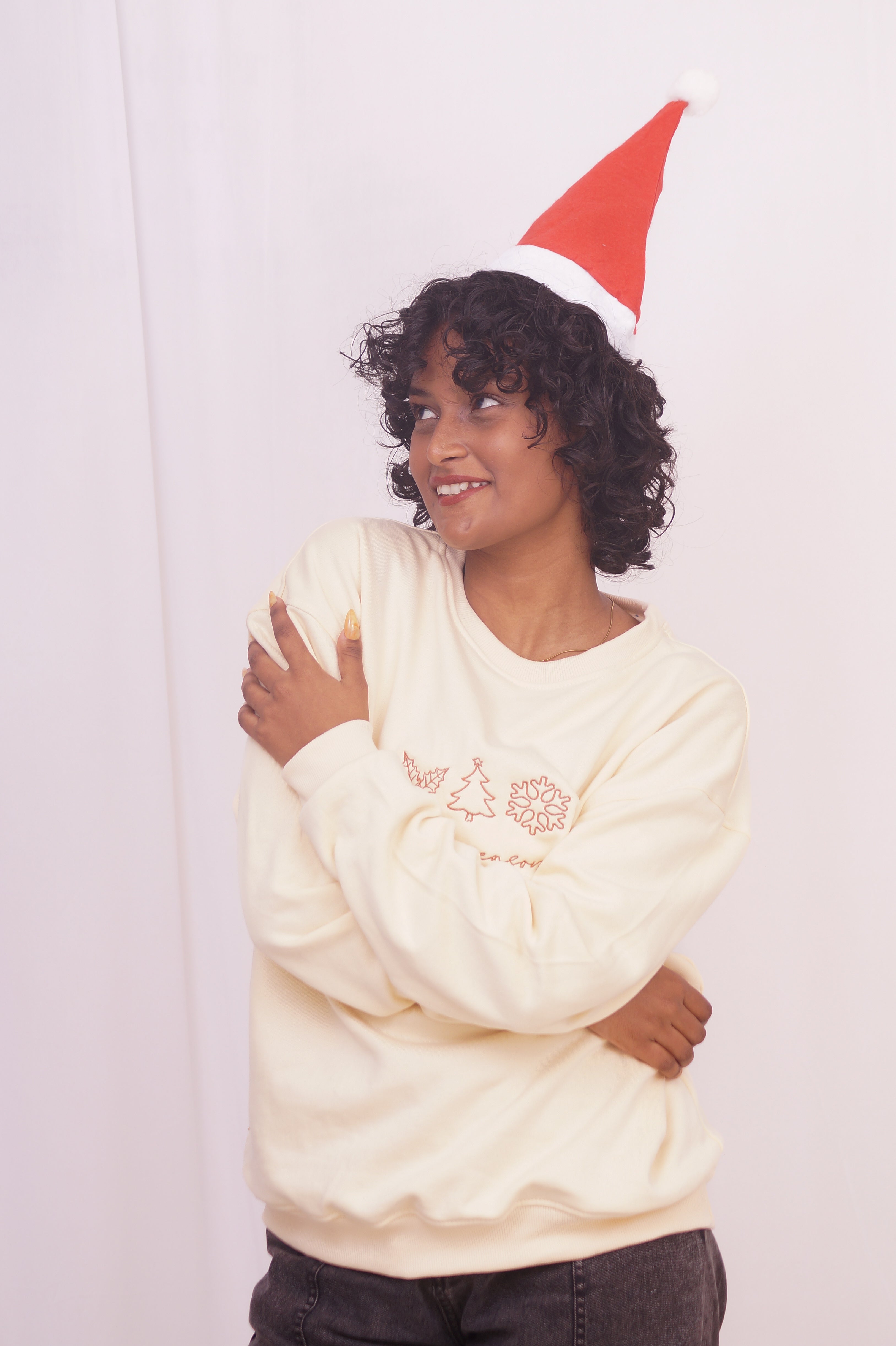 Person wearing a cream-colored sweatshirt with a floral design and a red Santa hat on a plain background