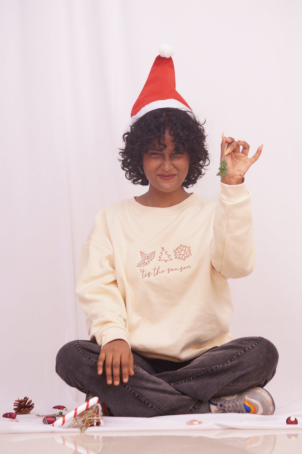 Person wearing a Santa hat and a white sweatshirt with text, sitting on a white background.