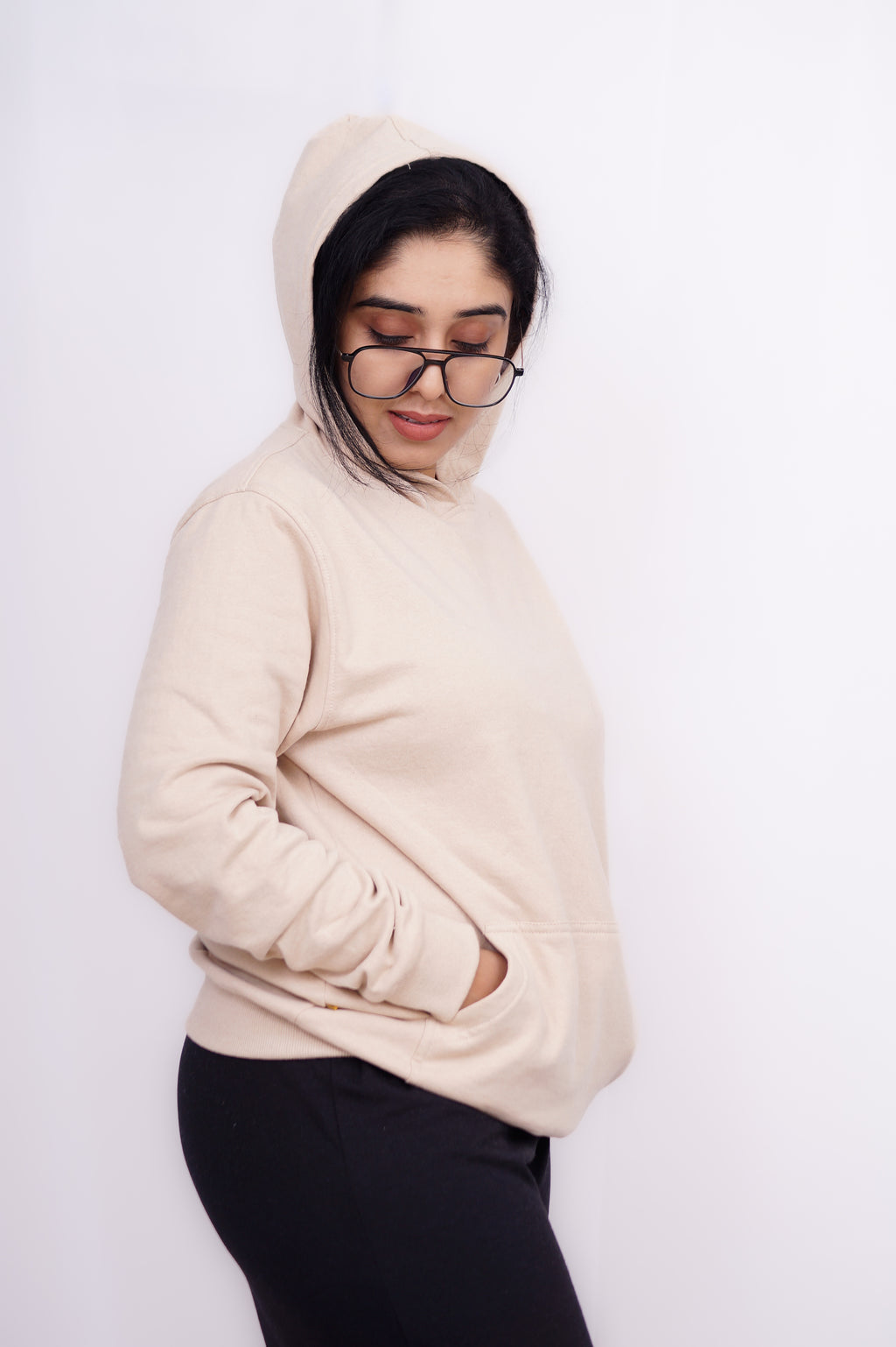 Person wearing a beige hoodie and black pants on a white background
