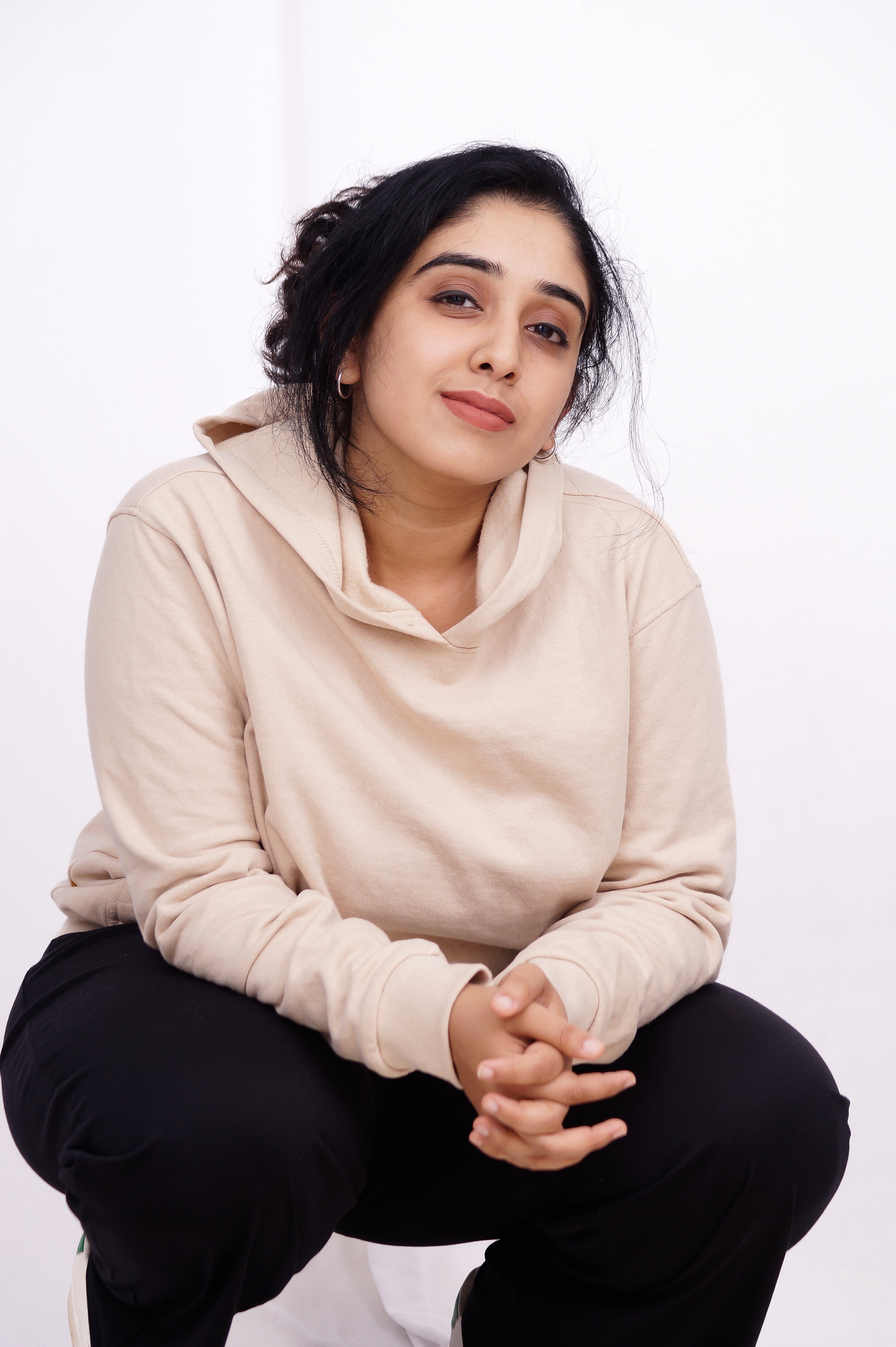 Woman wearing a beige sweater and black pants sitting on a white background