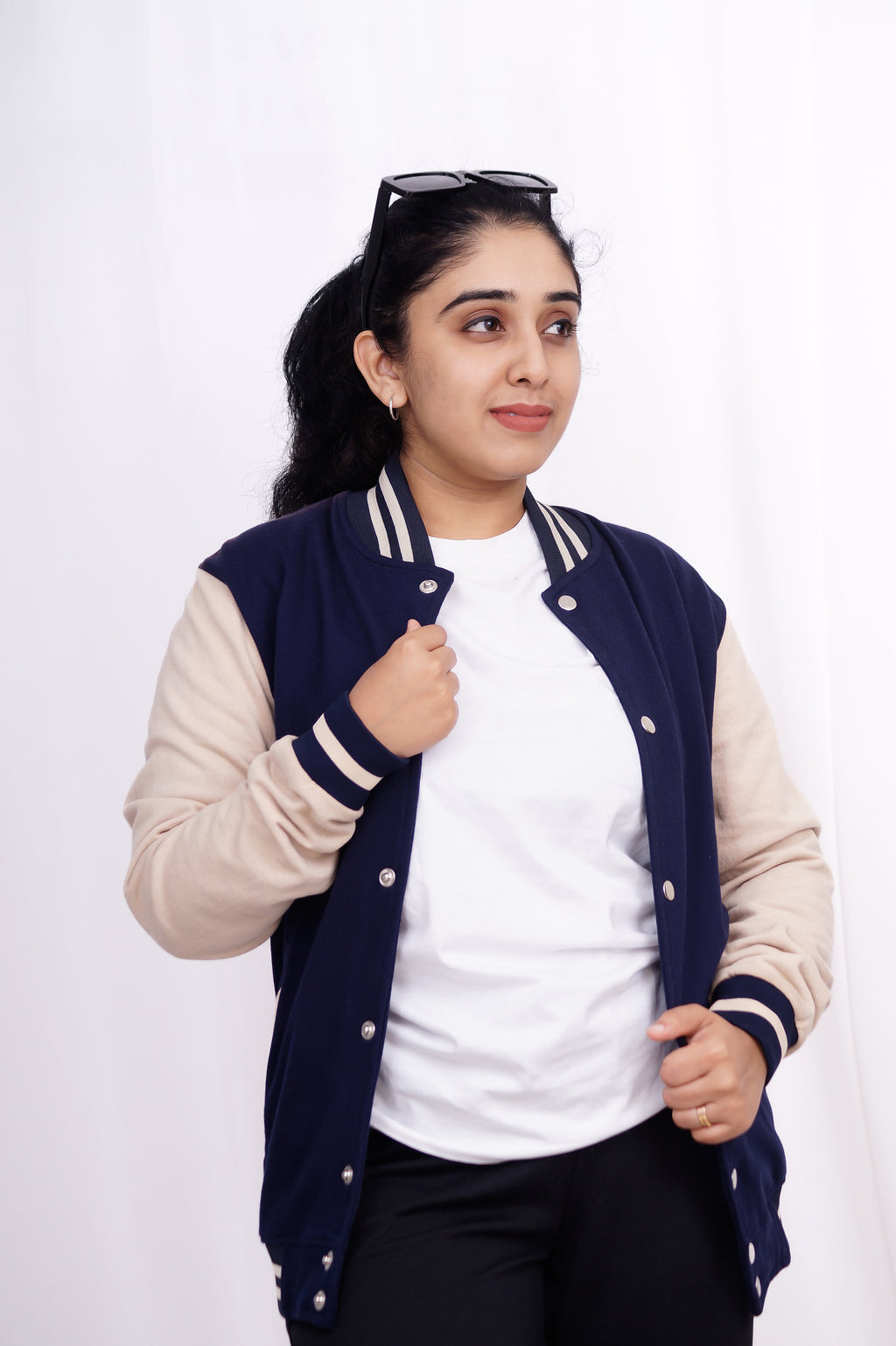 Woman wearing a navy blue and beige varsity jacket on a white background