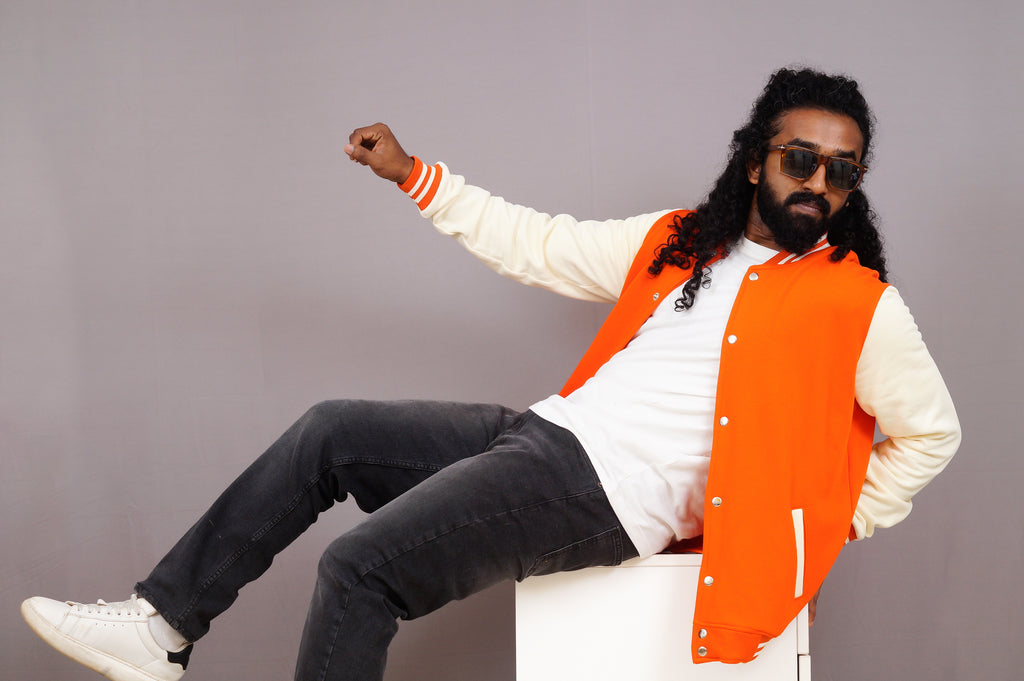 Man wearing an orange vest and sunglasses sitting on a chair against a gray background