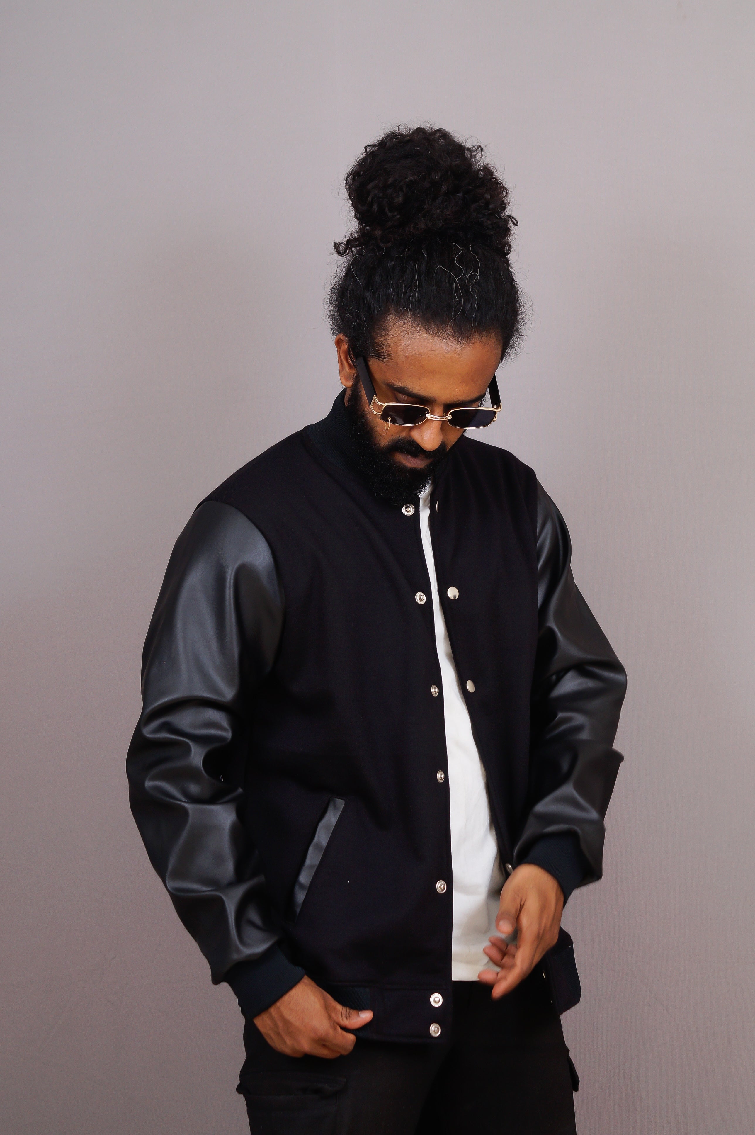 Man wearing a black varsity jacket with leather sleeves against a gray background