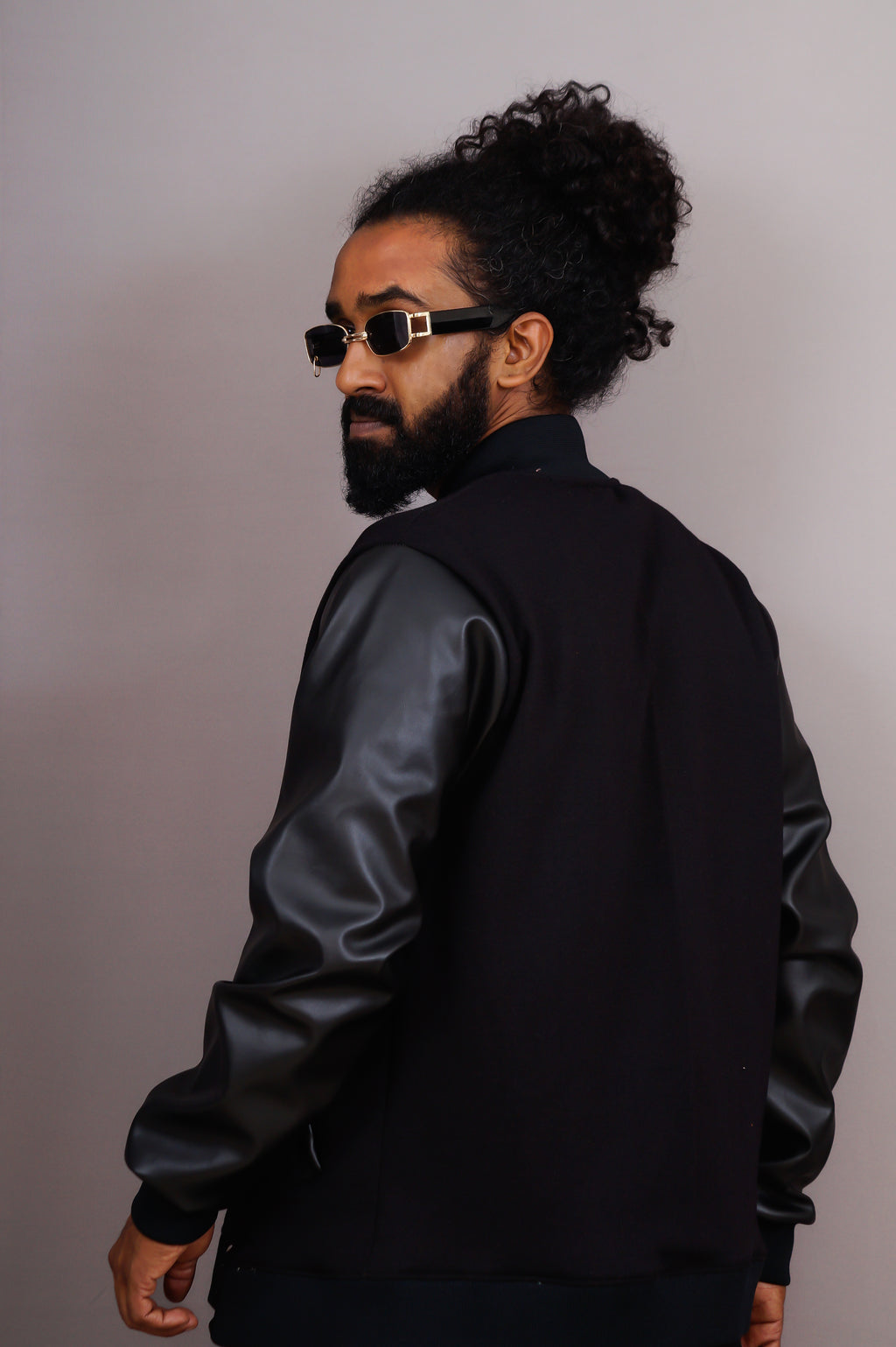Man wearing a black jacket with leather sleeves against a plain background