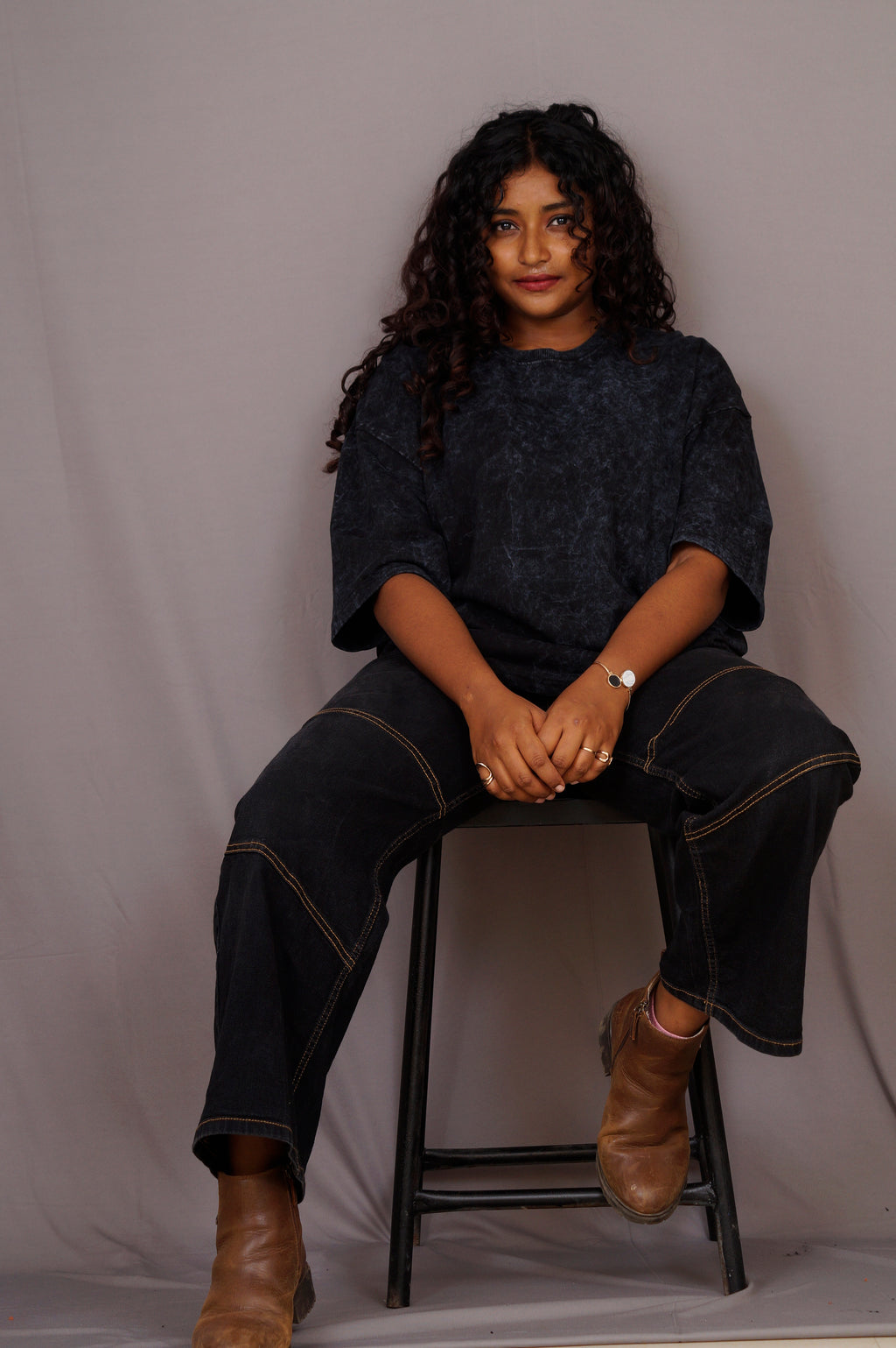 Person sitting on a stool against a plain background