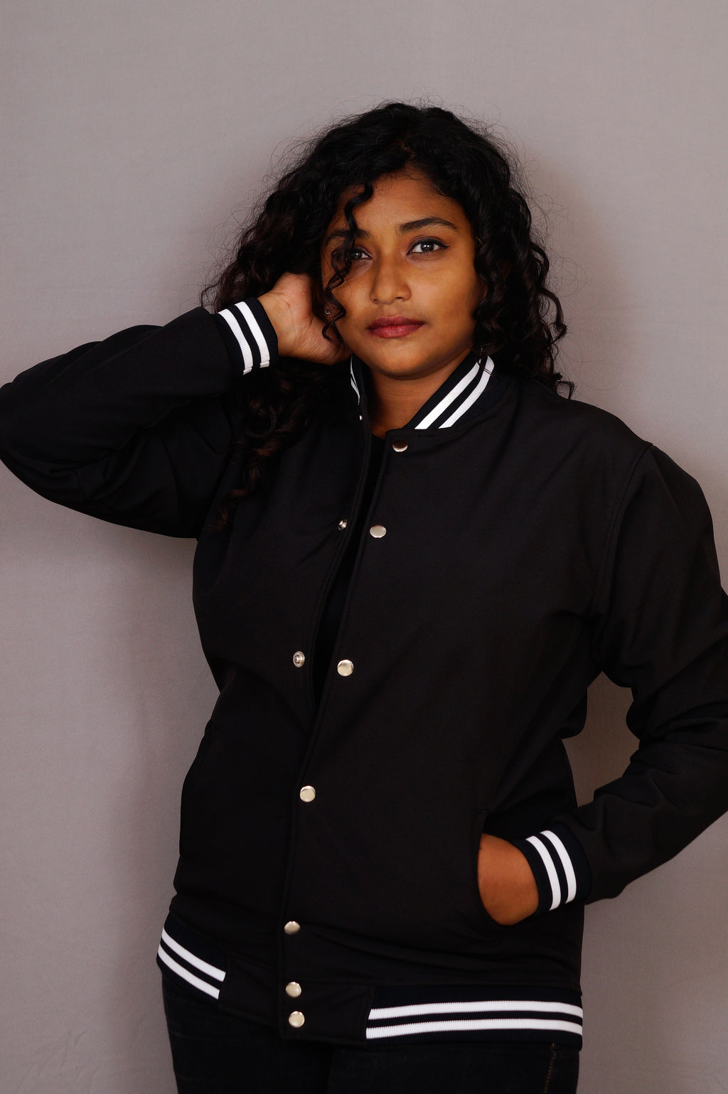 Person wearing a black varsity jacket with white stripes on a plain background
