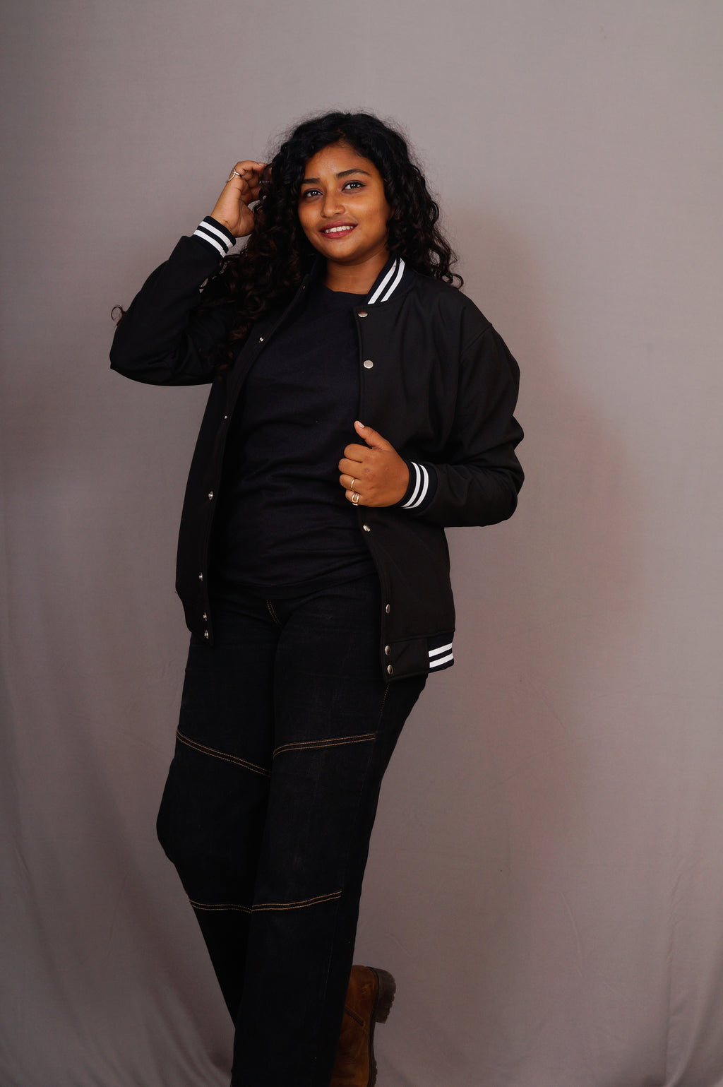 Person wearing a black varsity jacket with white stripes on a plain background