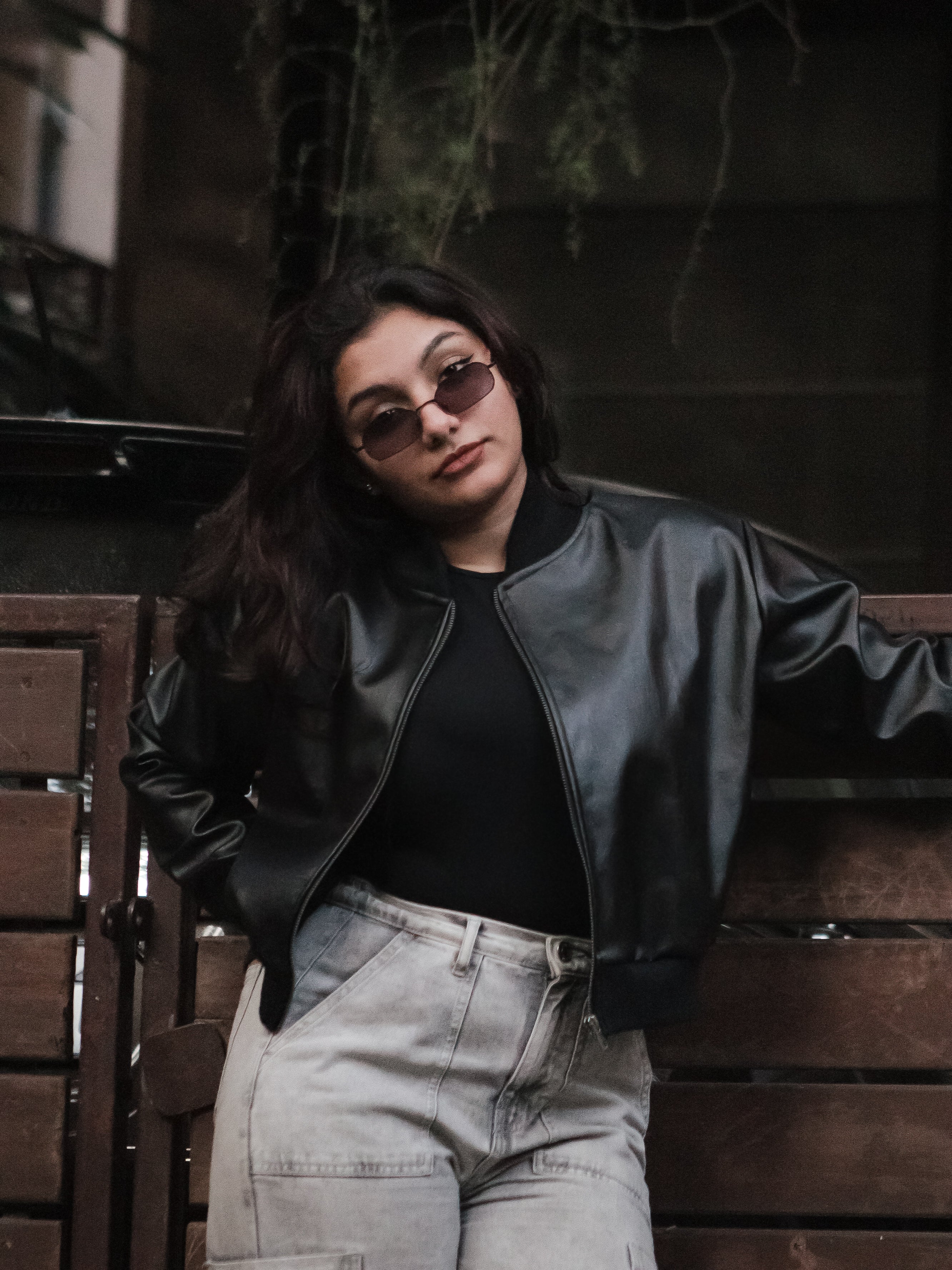 Person wearing a black leather jacket and sunglasses against a dark background
