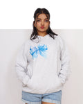 Person wearing a white sweatshirt with a blue bow design on a plain background