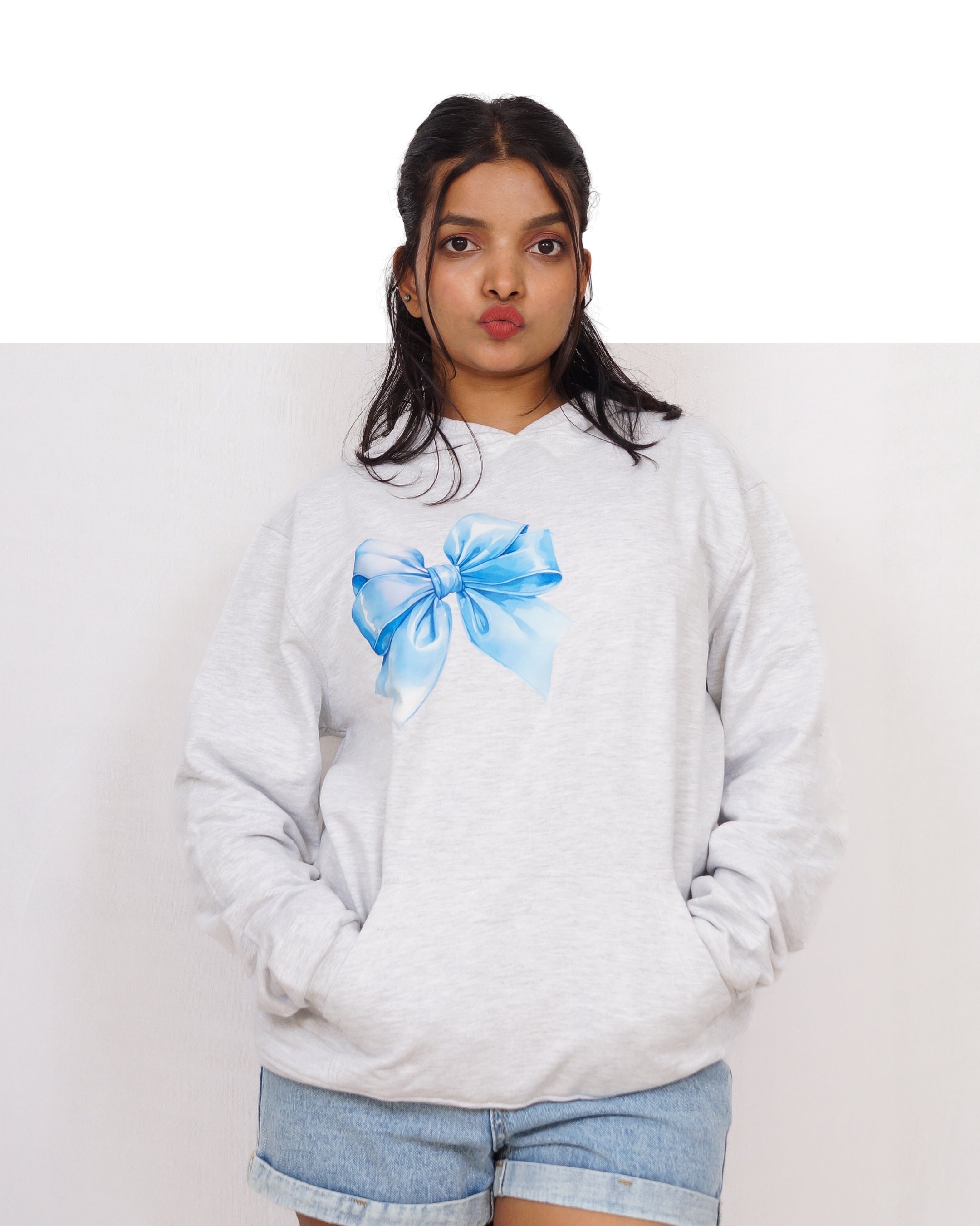 Person wearing a white sweatshirt with a blue bow design on a plain background