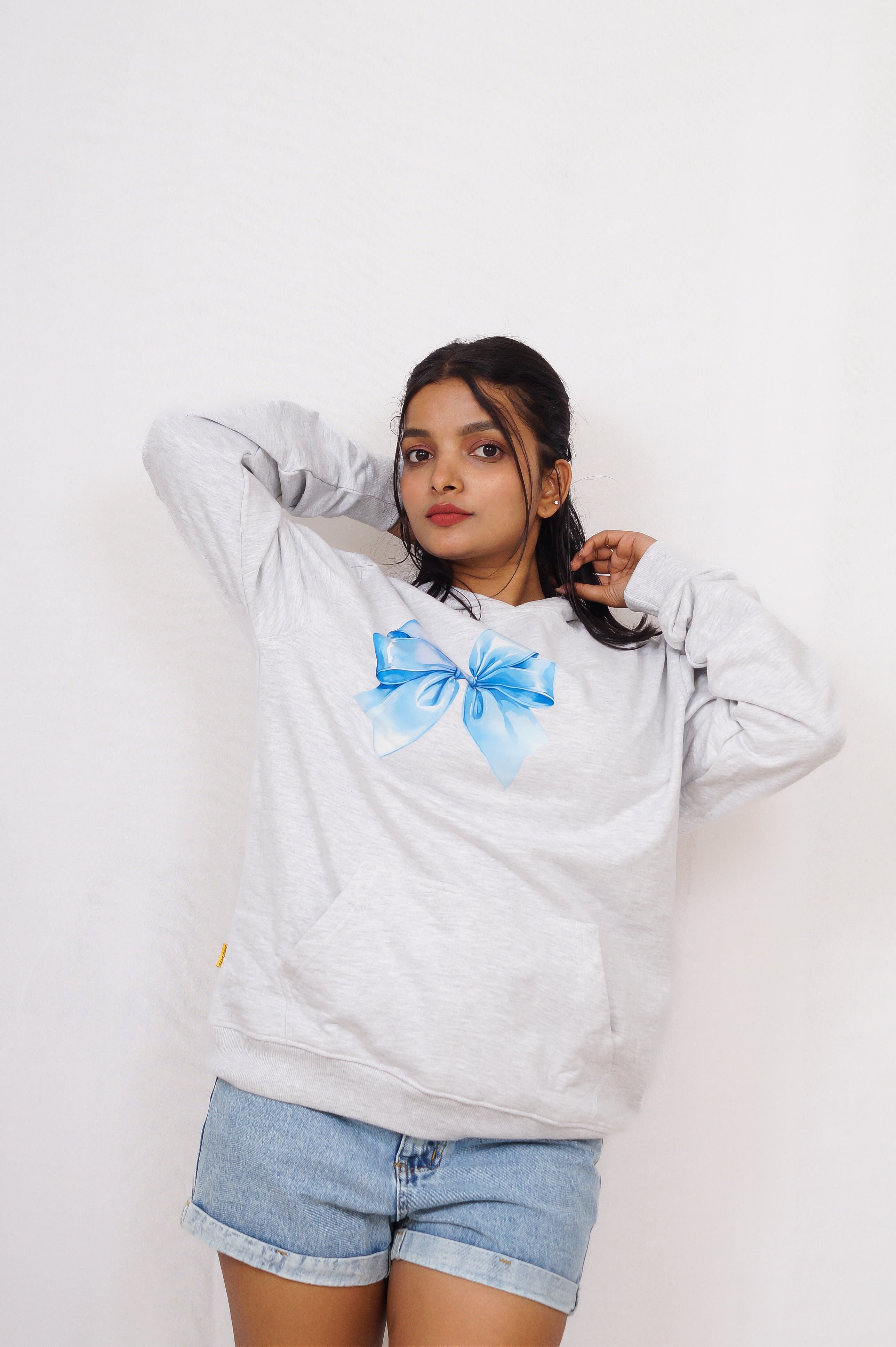 Person wearing a light gray sweatshirt with a blue bow design on a white background