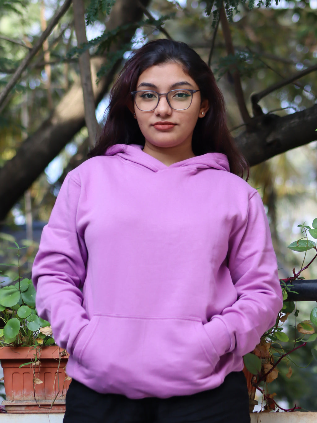Person wearing a purple hoodie standing outdoors with greenery in the background