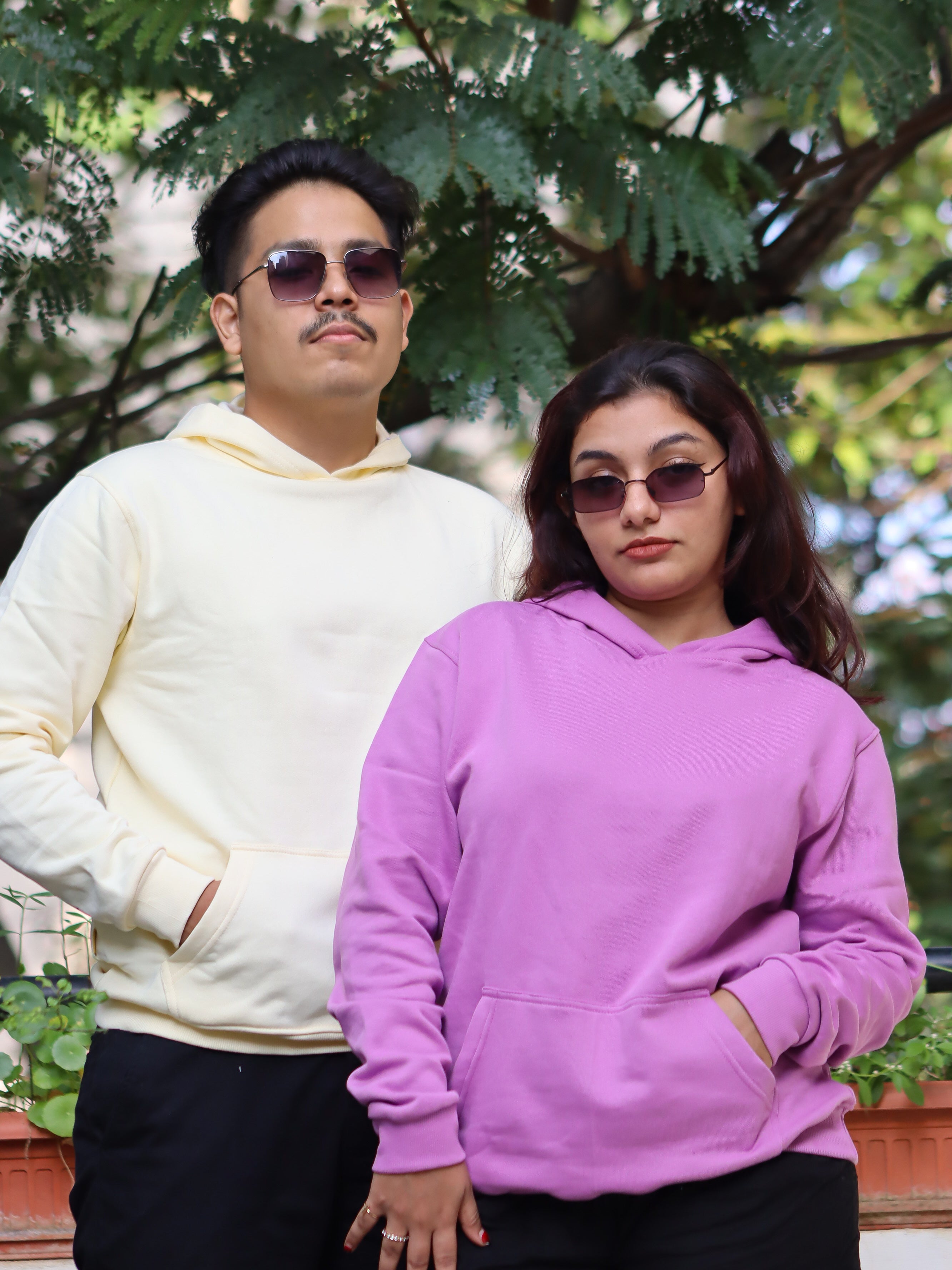 Two people wearing hoodies standing outdoors with greenery in the background