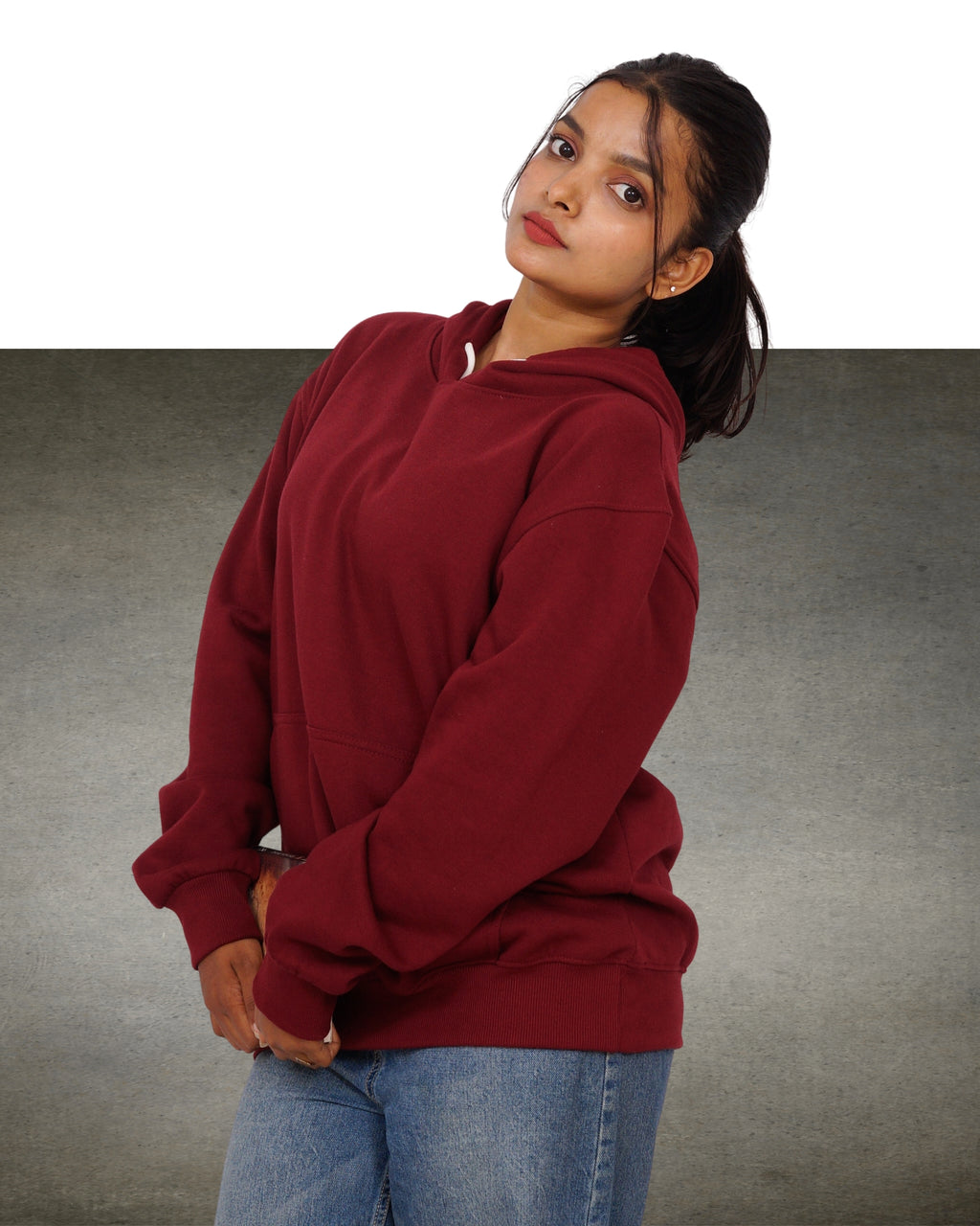 Person wearing a maroon hoodie and blue jeans on a gray background