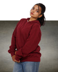 Person wearing a maroon hoodie and blue jeans on a gray background