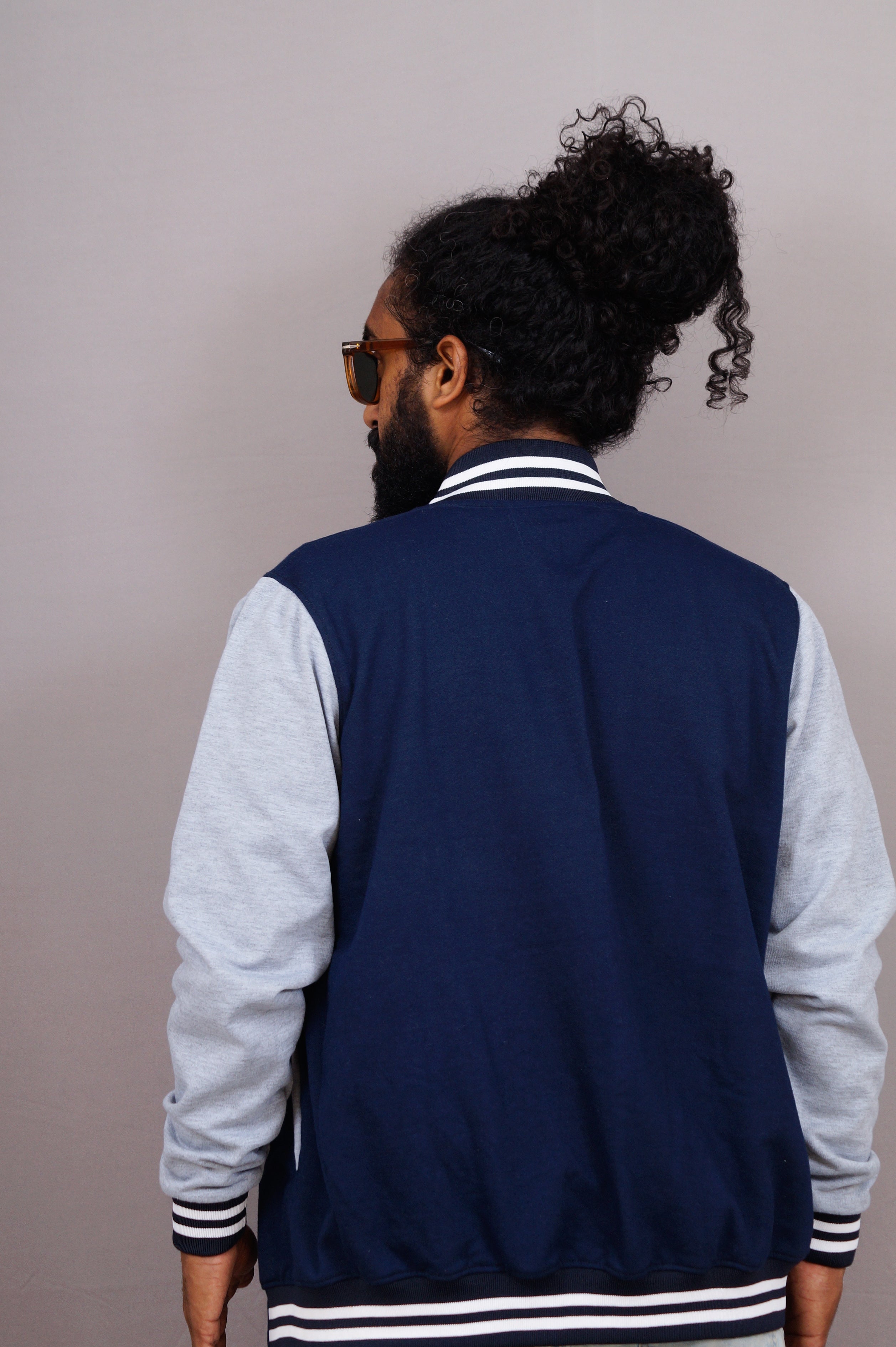 Man wearing a navy blue varsity jacket with white sleeves against a plain background