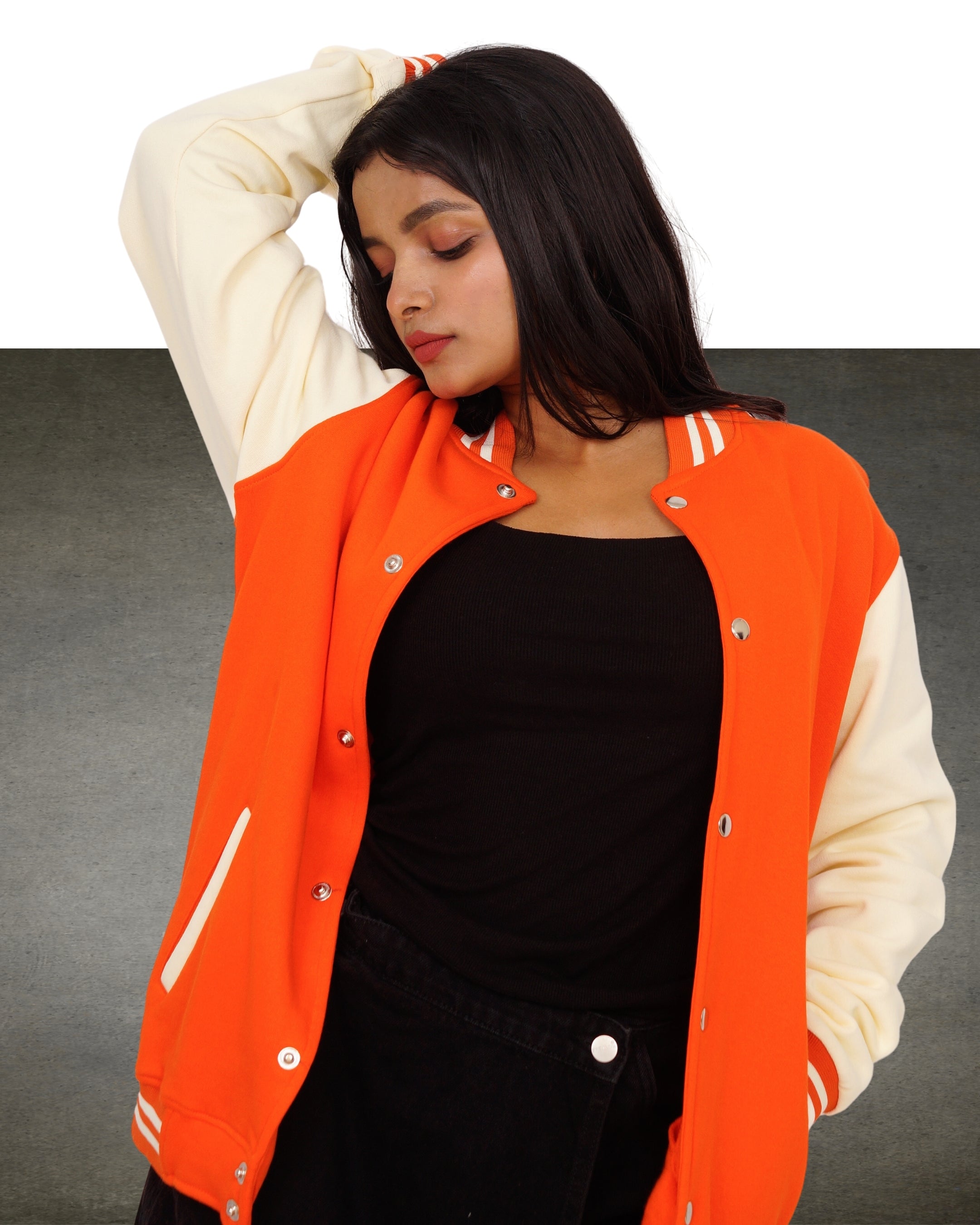 Person wearing a bright orange and white varsity jacket on a gray background