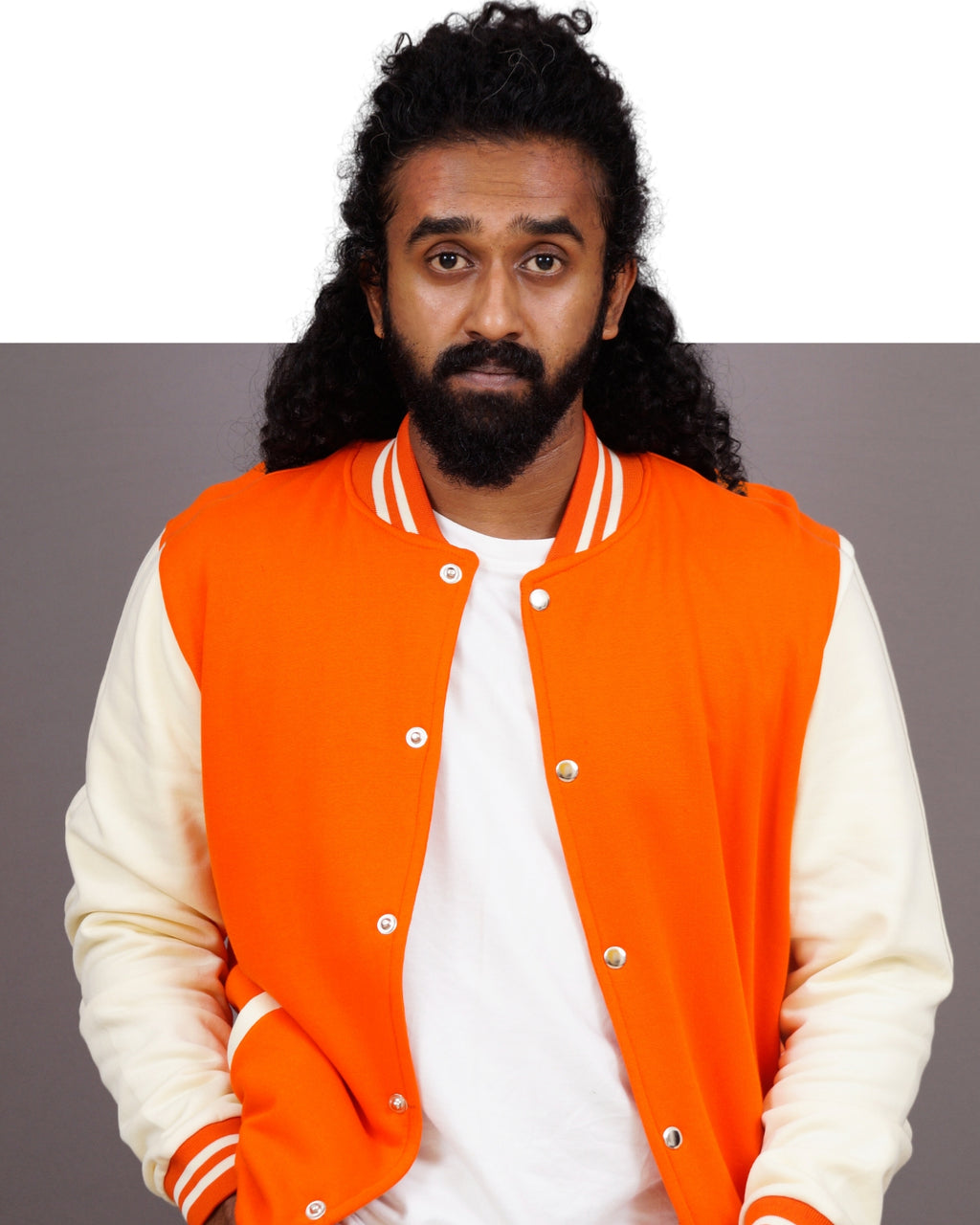 Person wearing an orange varsity jacket over a white shirt on a gray background