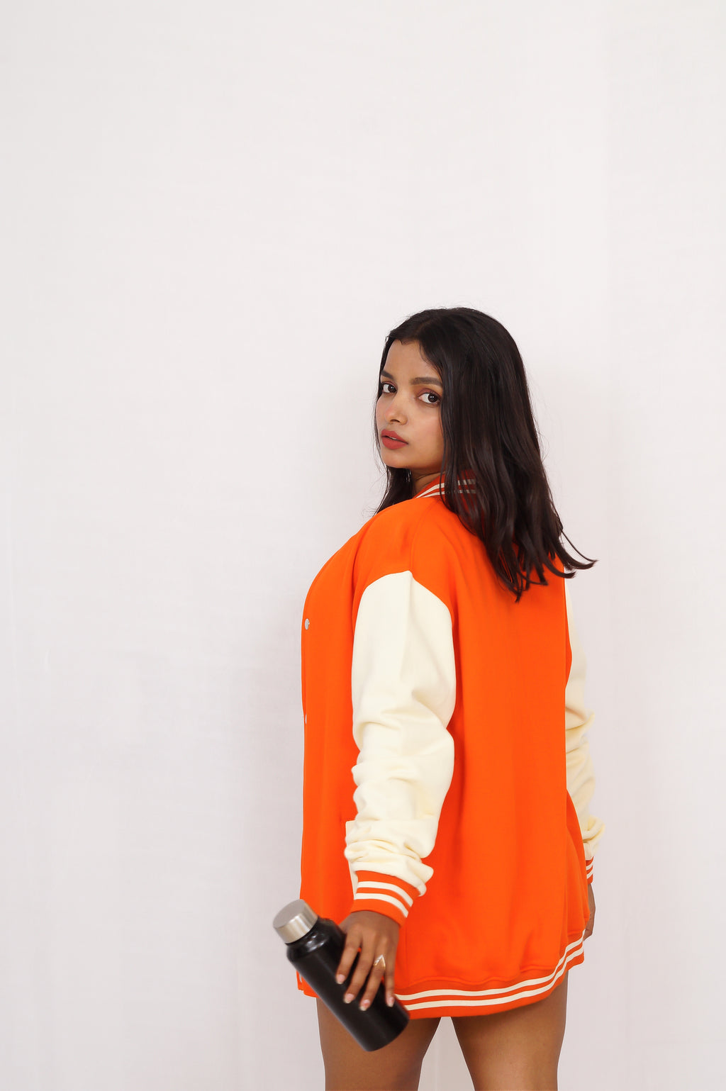 Person wearing an orange and white varsity jacket holding a water bottle against a plain background