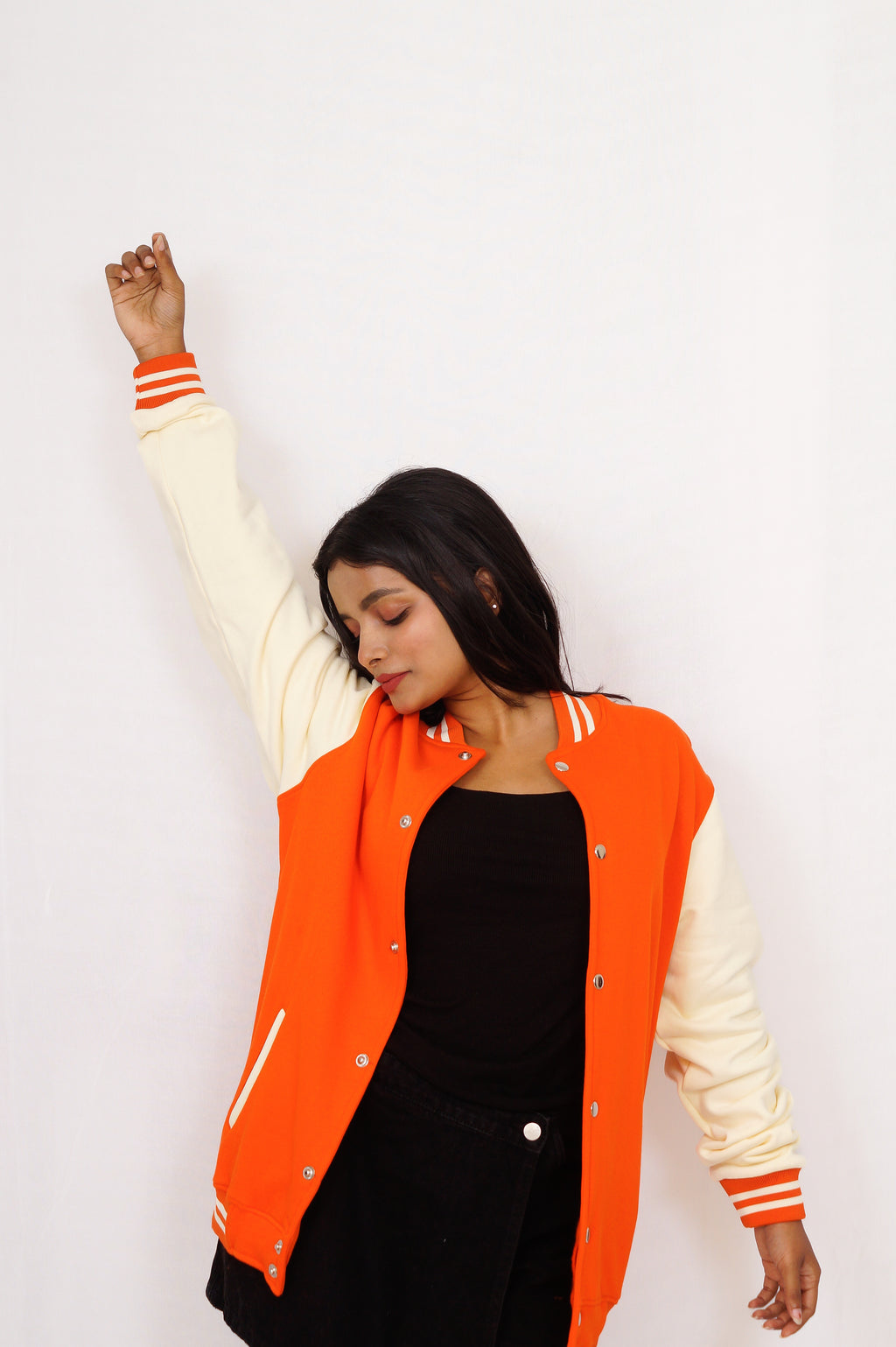 Person wearing an orange and white varsity jacket on a plain background