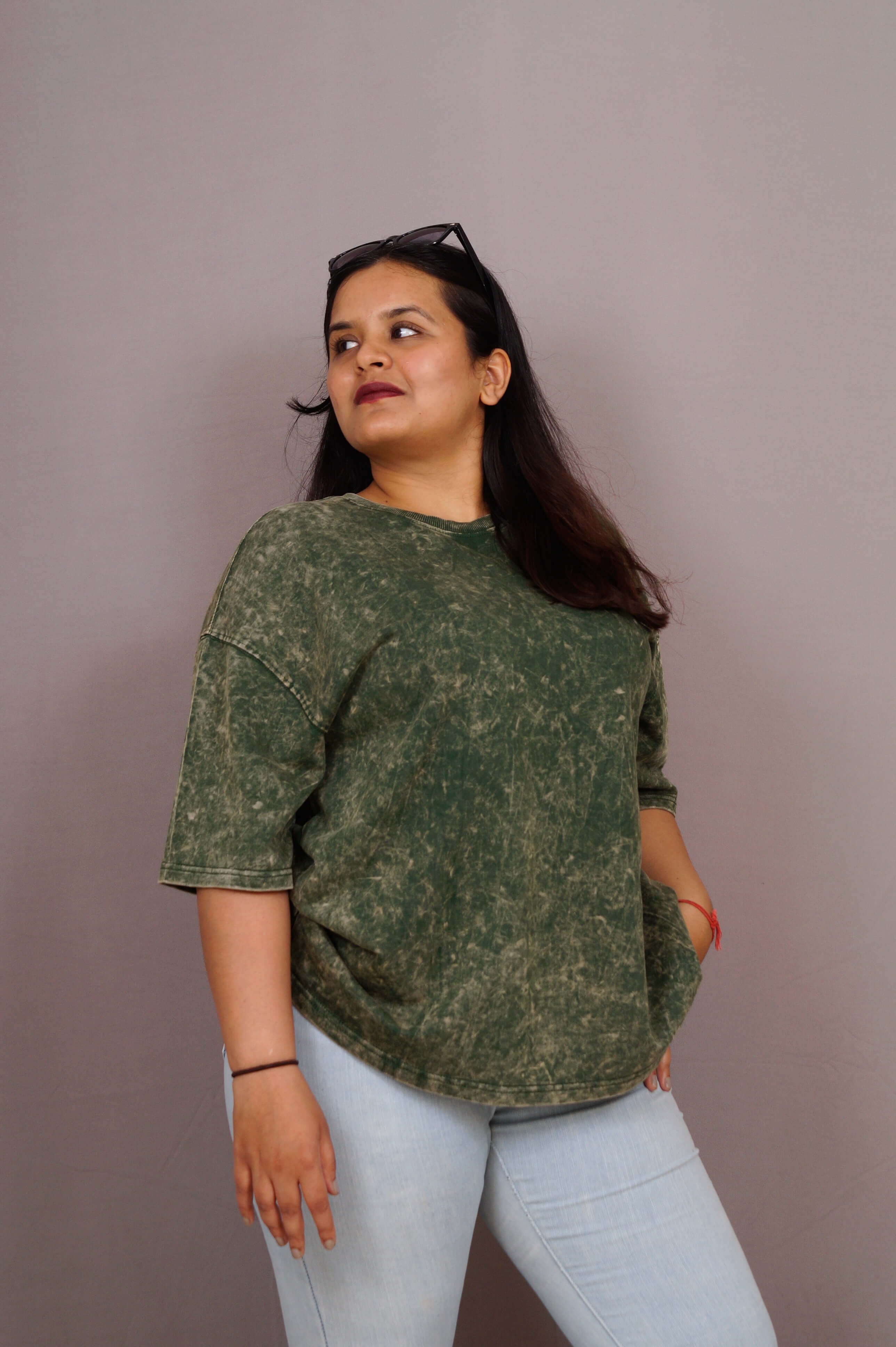 Woman wearing a green patterned shirt and light blue jeans against a plain background