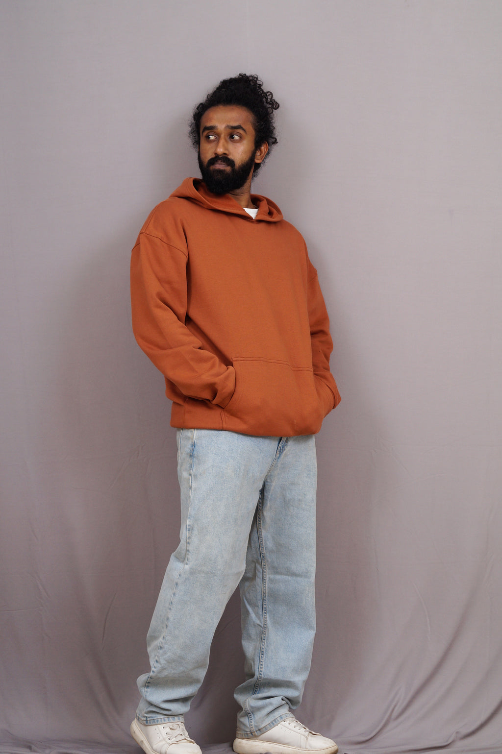 Man wearing an orange hoodie and light blue jeans against a plain background