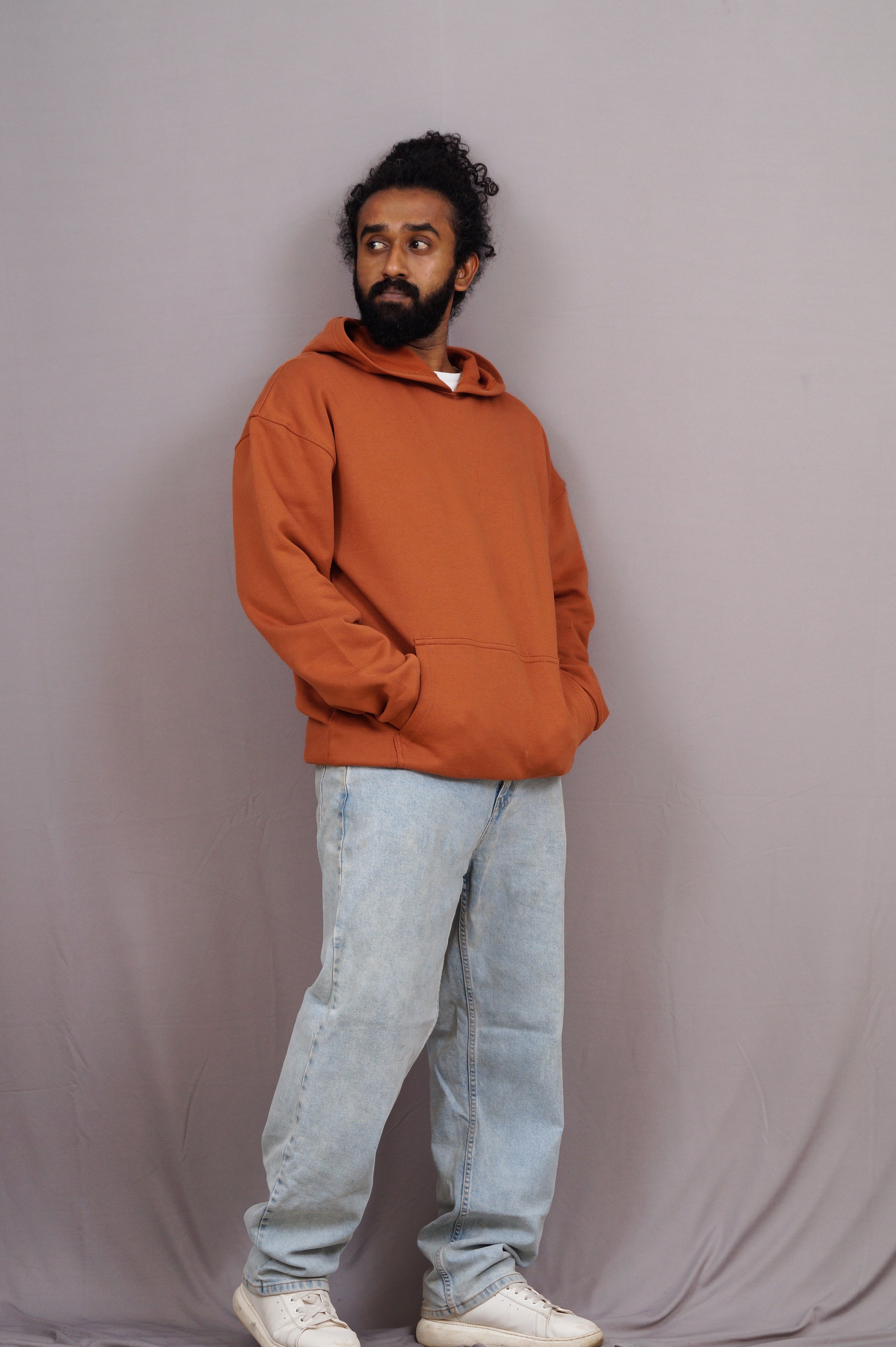 Man wearing an orange hoodie and light blue jeans against a plain background