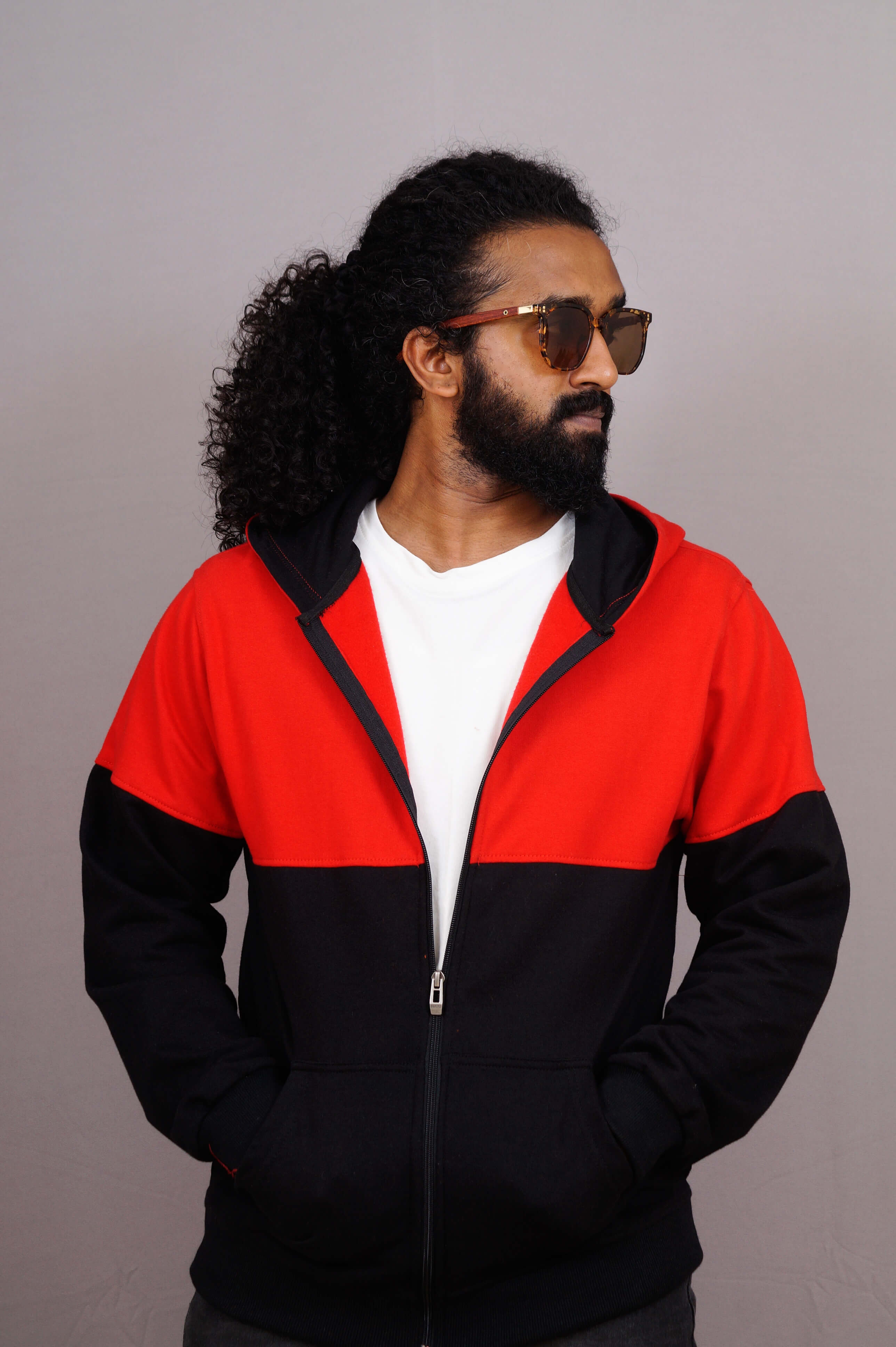 Man wearing a red and black jacket with sunglasses on a plain background