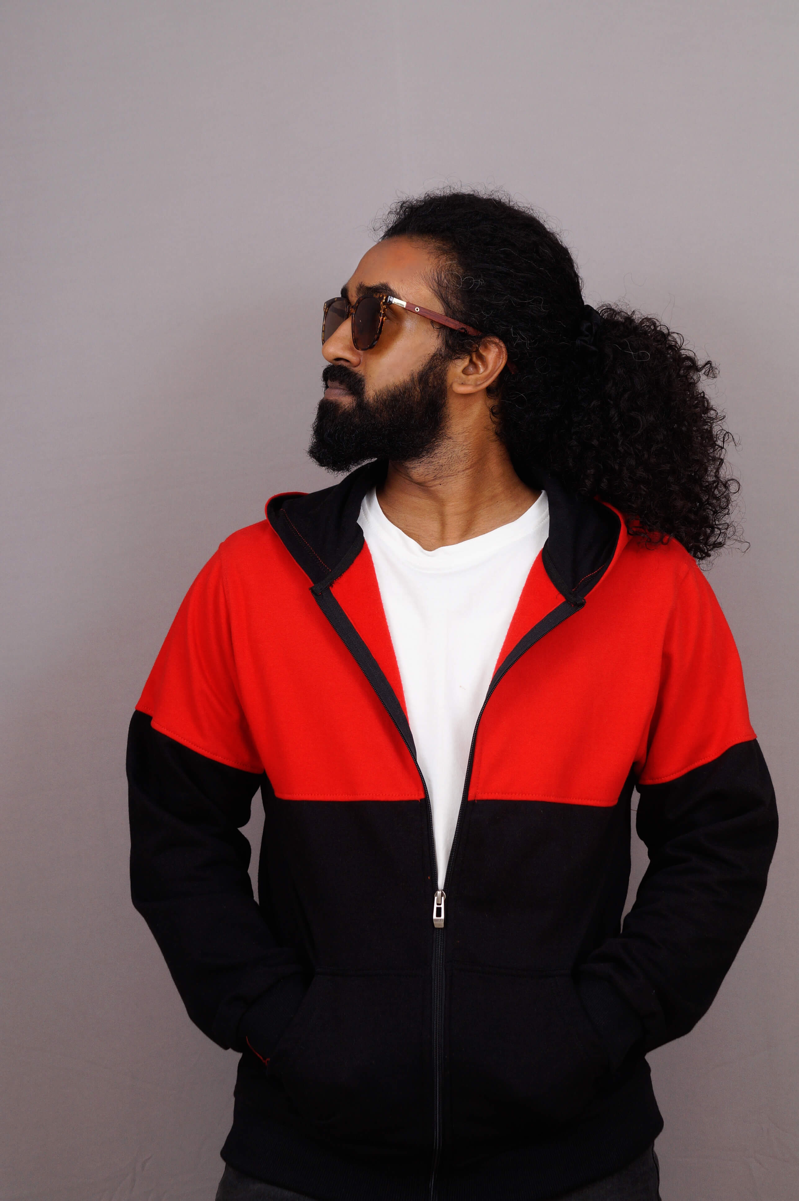 Man wearing a red and black jacket with sunglasses on a plain background