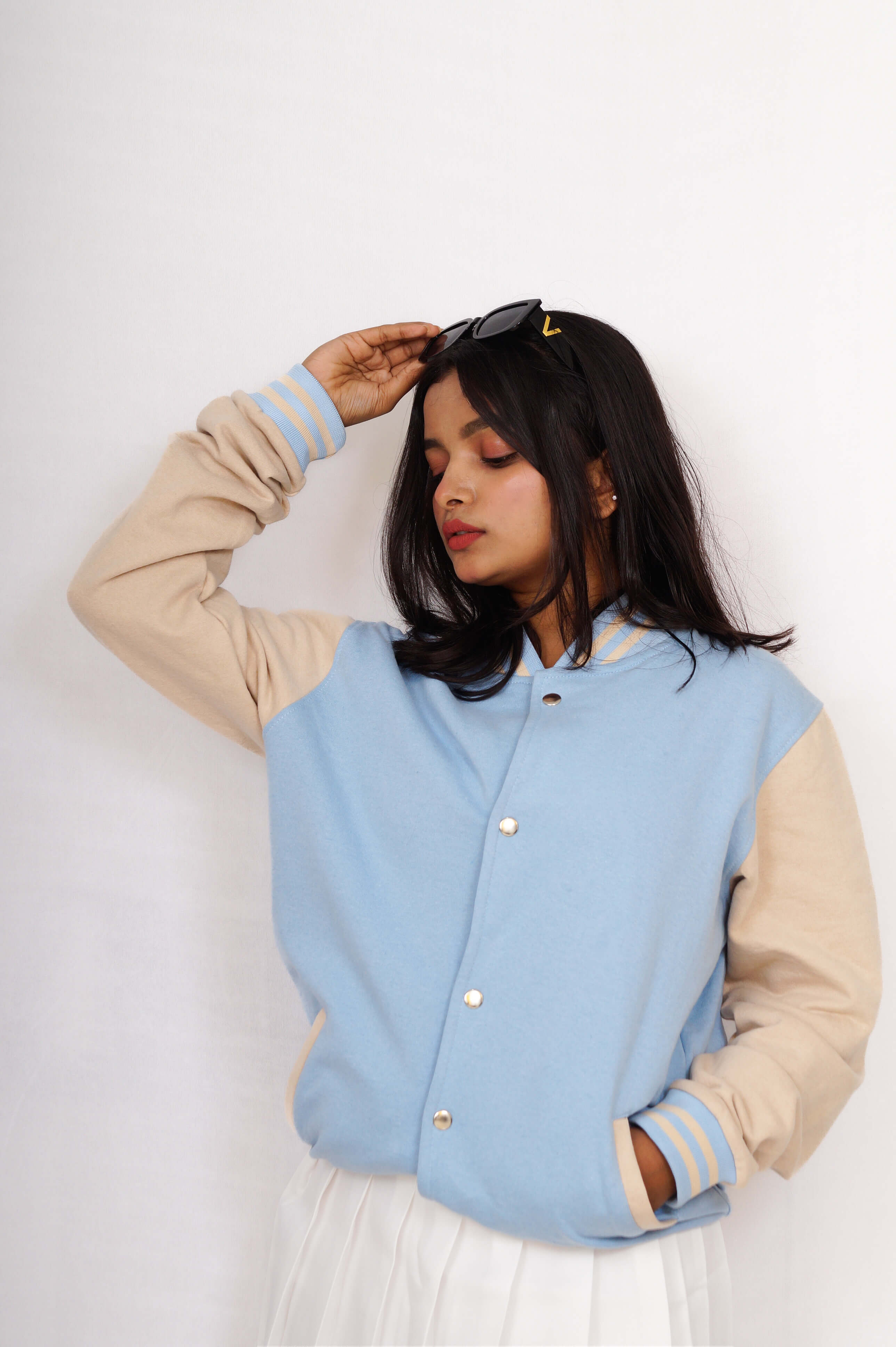 Woman wearing a light blue and beige varsity jacket on a white background