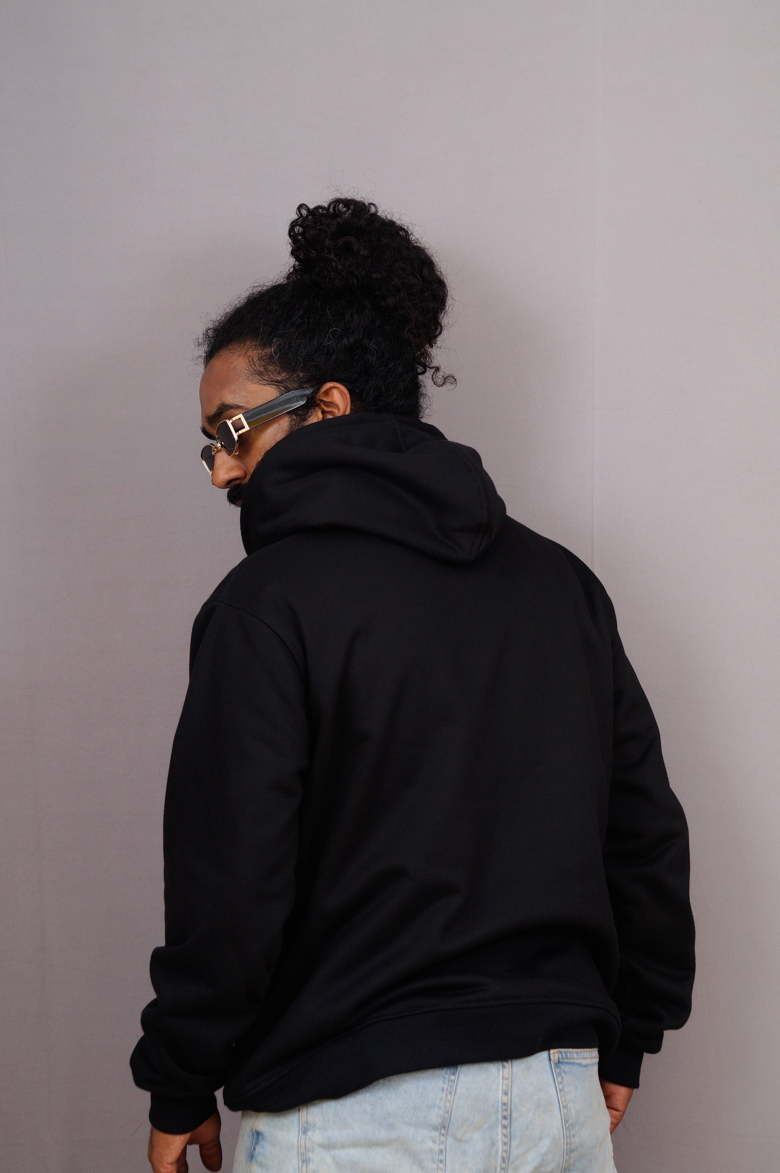 Person wearing a black hoodie and light blue jeans against a plain background