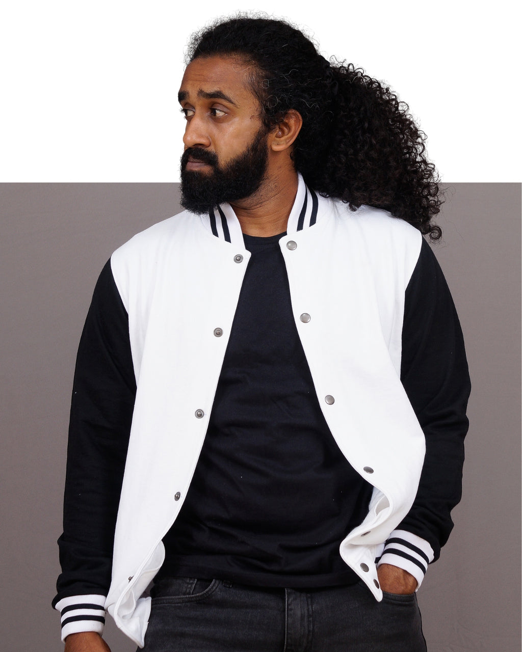 Man wearing a black and white varsity jacket against a gray background