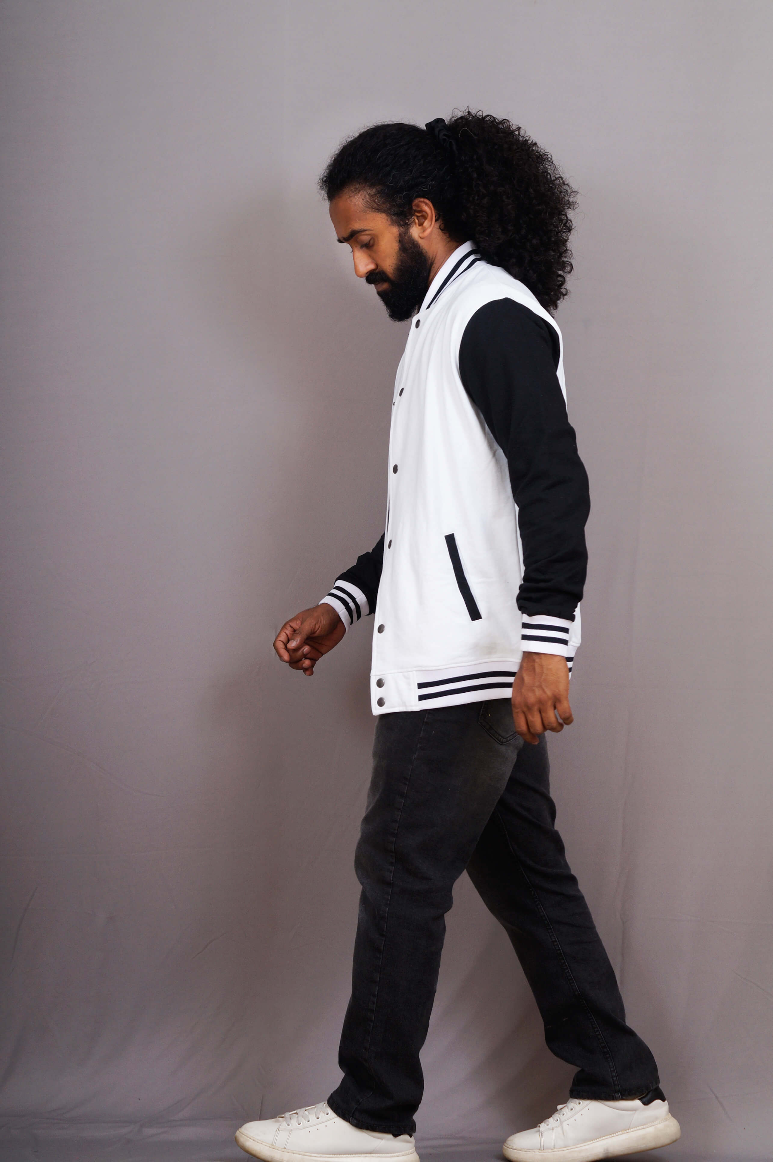 Man wearing a white and black varsity jacket walking against a gray background