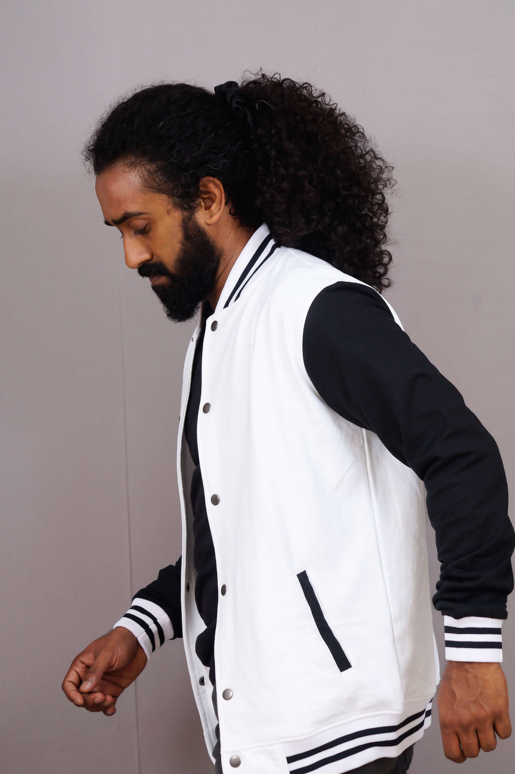 Man wearing a white varsity jacket with black sleeves against a plain background