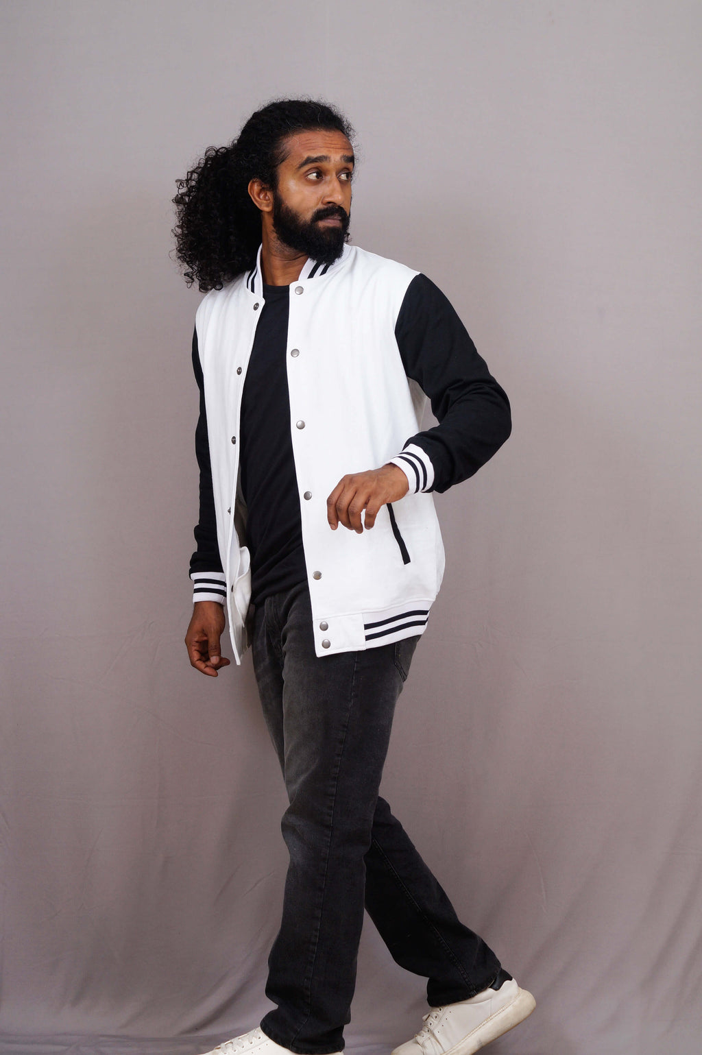 Man wearing a white varsity jacket with black sleeves and pants on a gray background