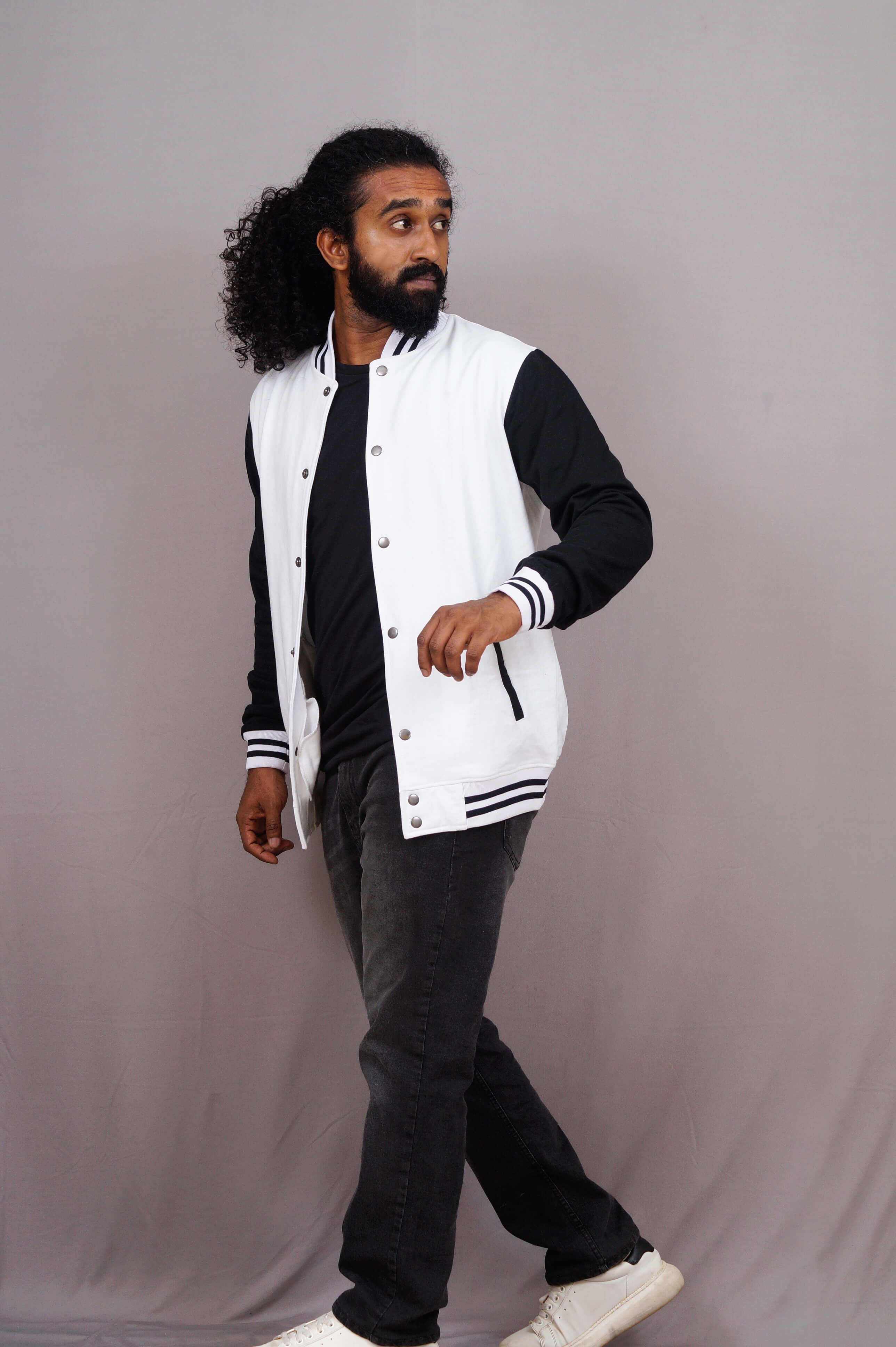 Man wearing a white varsity jacket with black sleeves and pants on a gray background