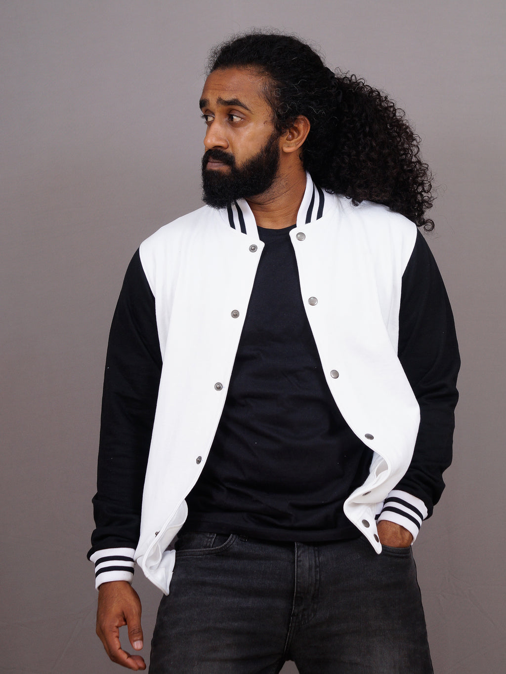 Man wearing a black and white varsity jacket against a gray background
