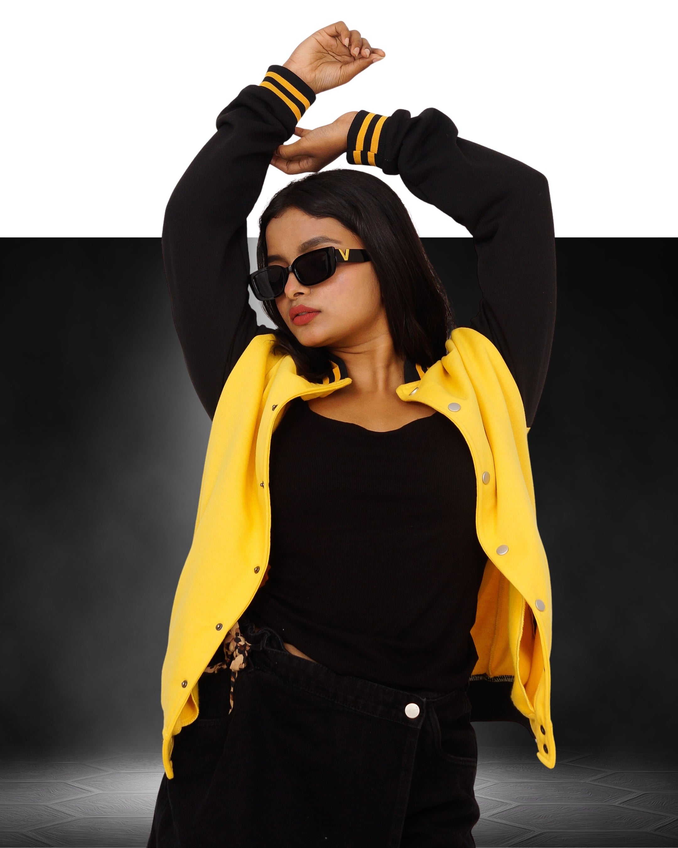 Person wearing a black outfit with a yellow varsity jacket on a dark background