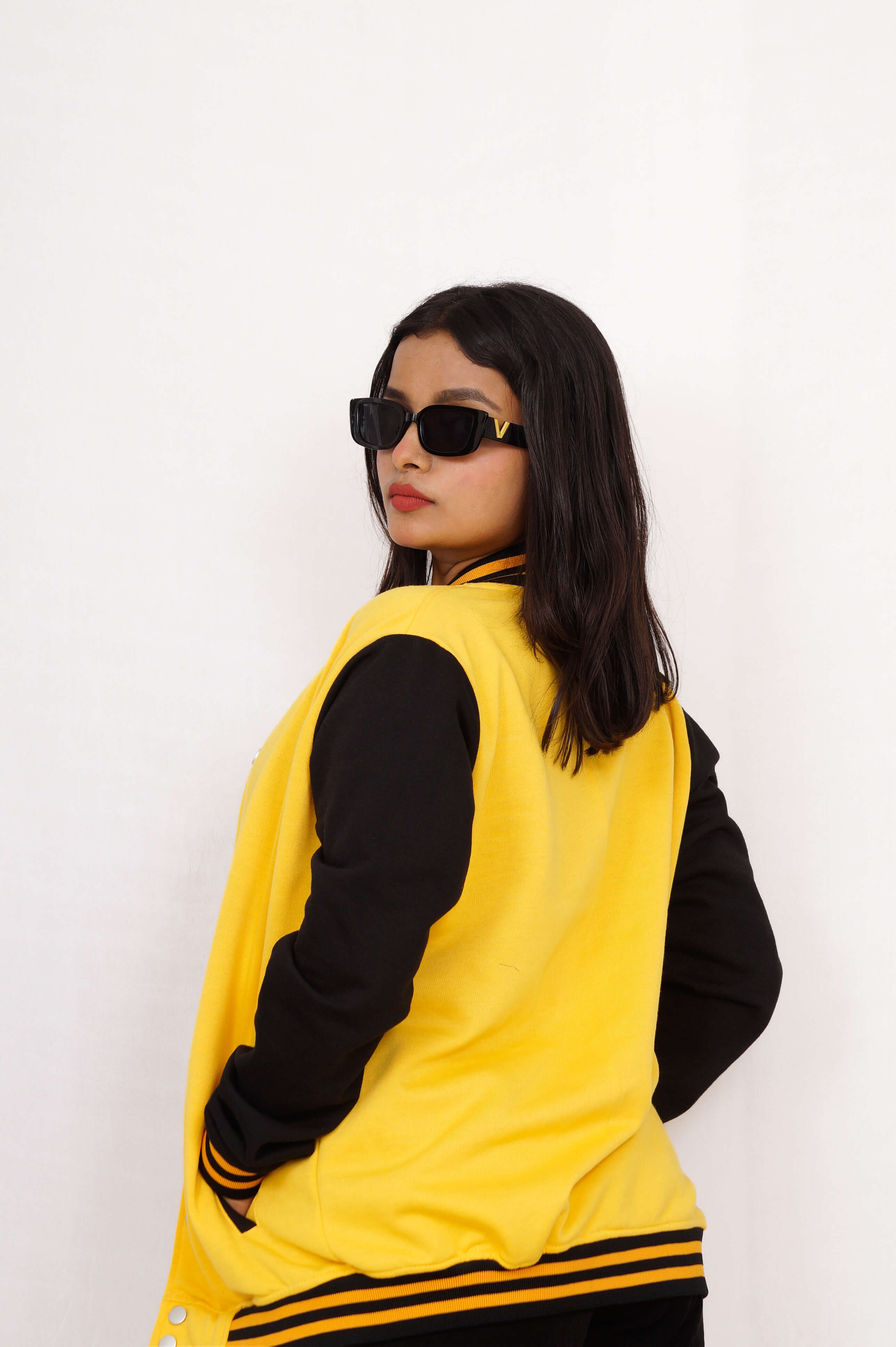 Person wearing a yellow and black varsity jacket with sunglasses on a white background